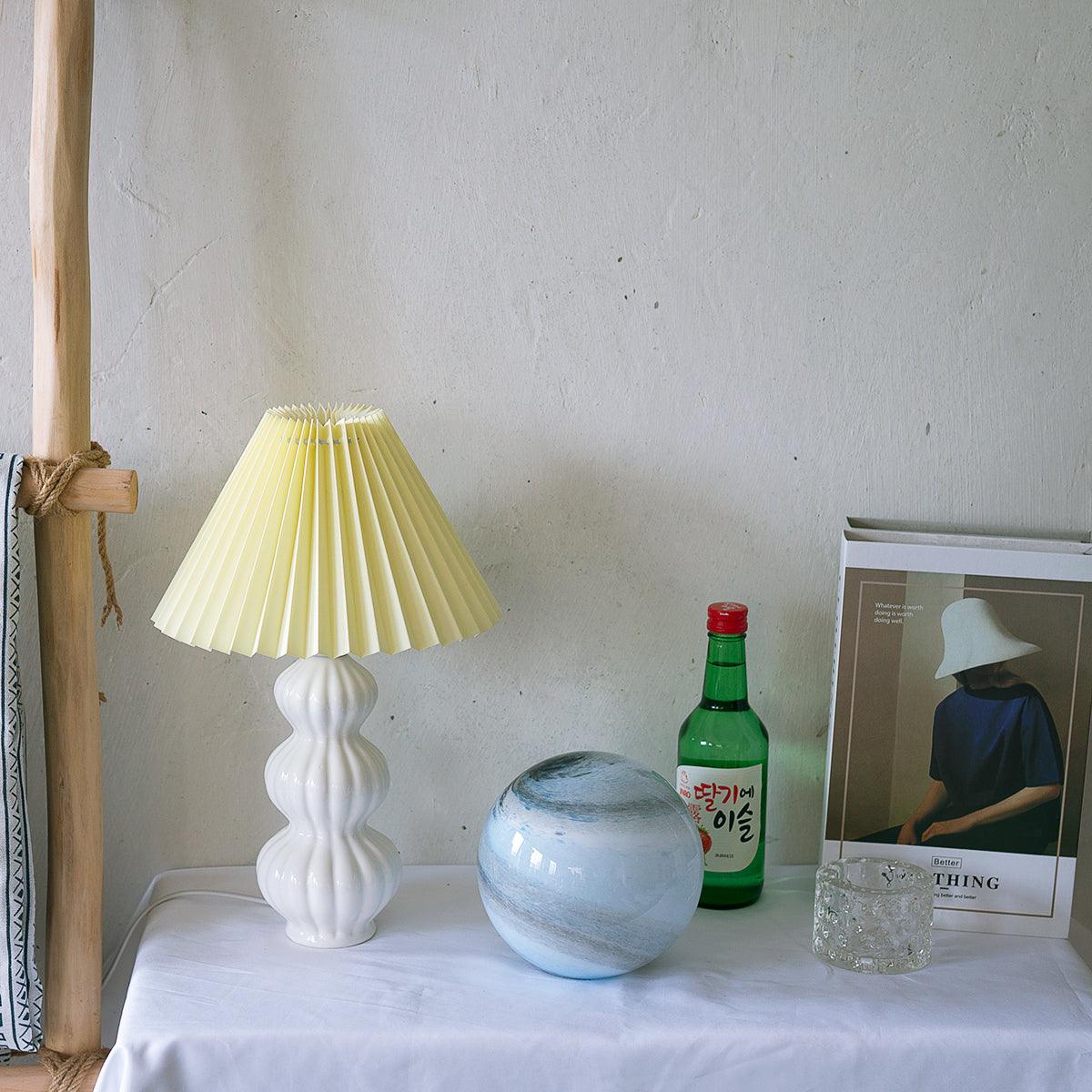 Leo lamp with a pale yellow pleated shade beside a blue ceramic bowl