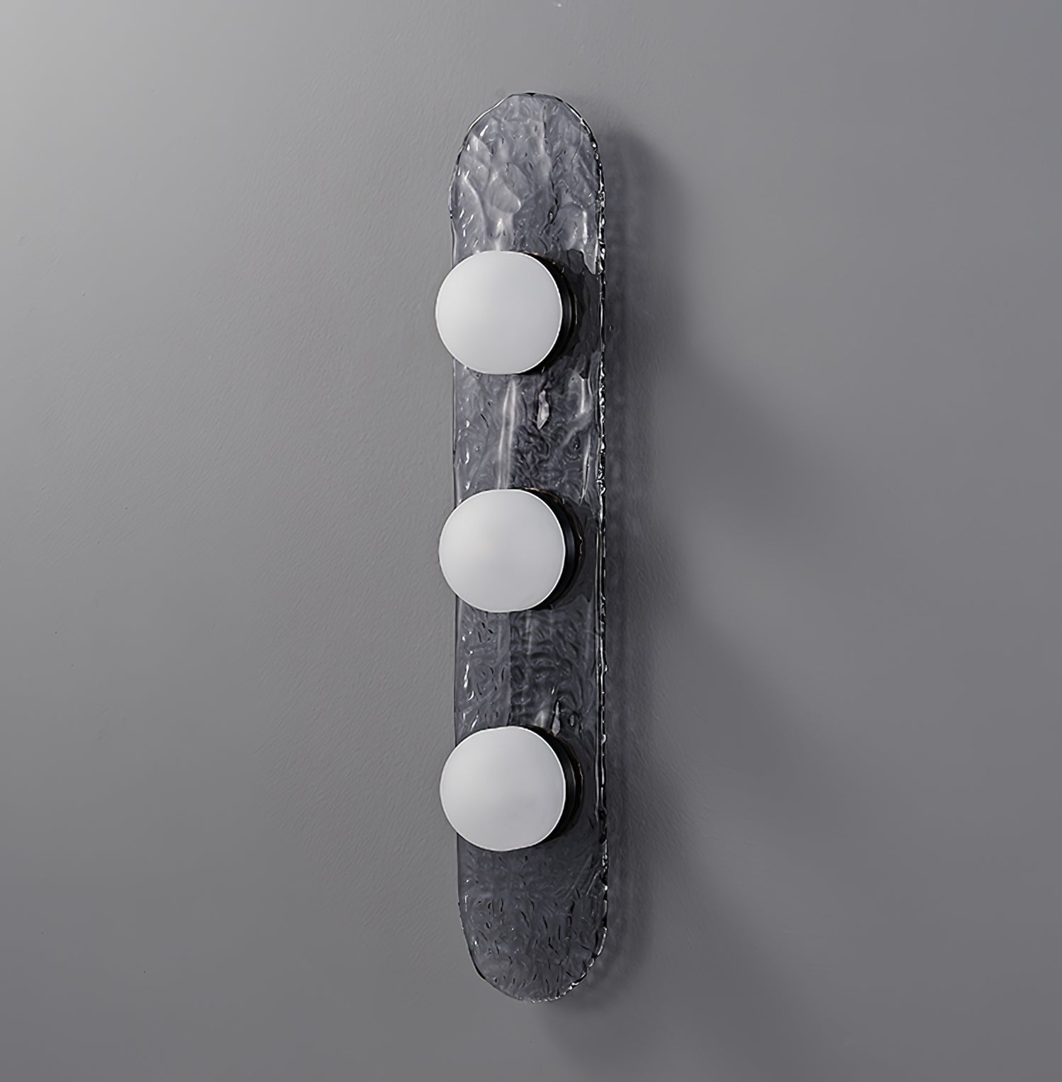 Unlit three-dome Modulo wall light on elongated rippled grey glass against a grey wall
