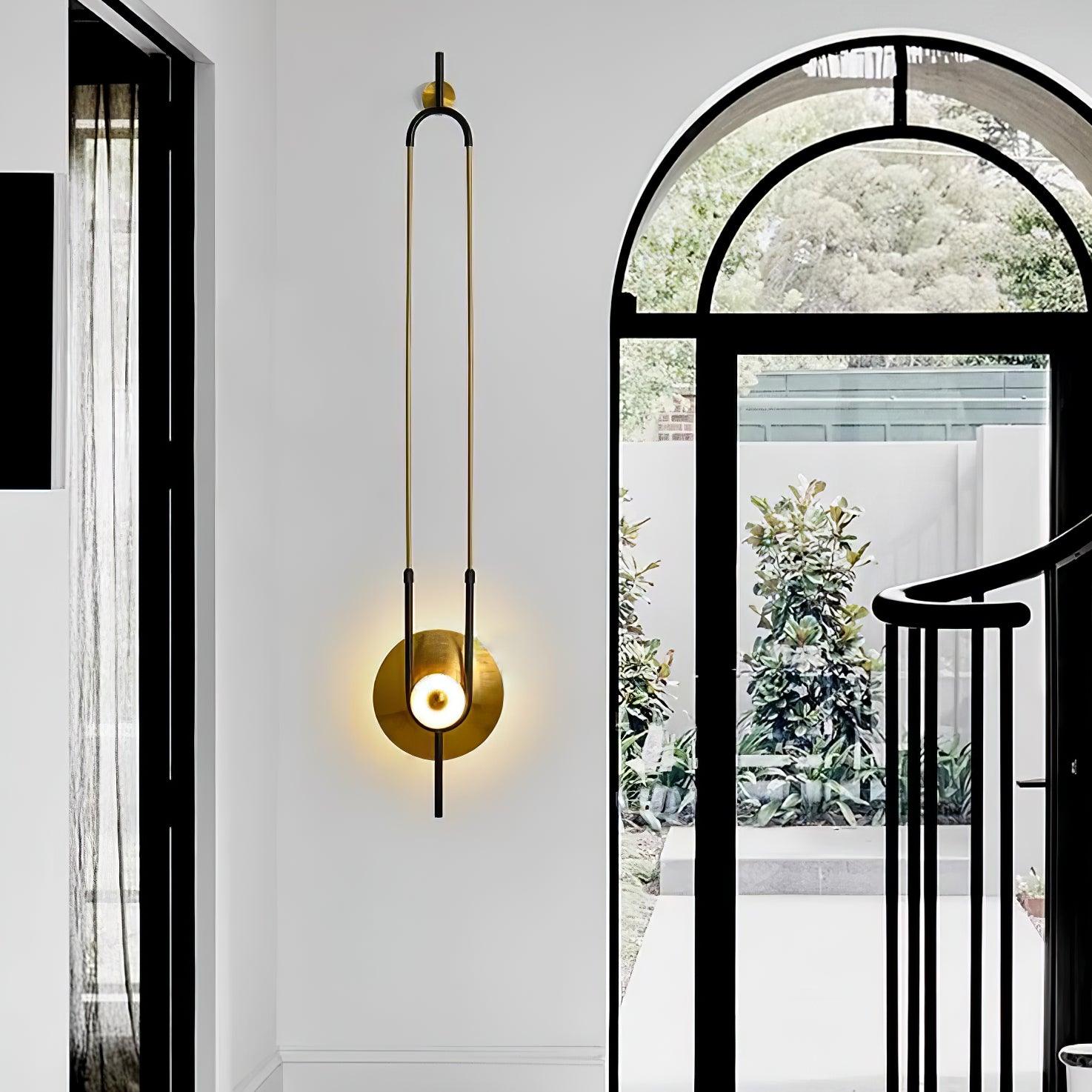 Ellipse Ring wall light beside black arched window and curved stair railing, with foliage beyond the glass