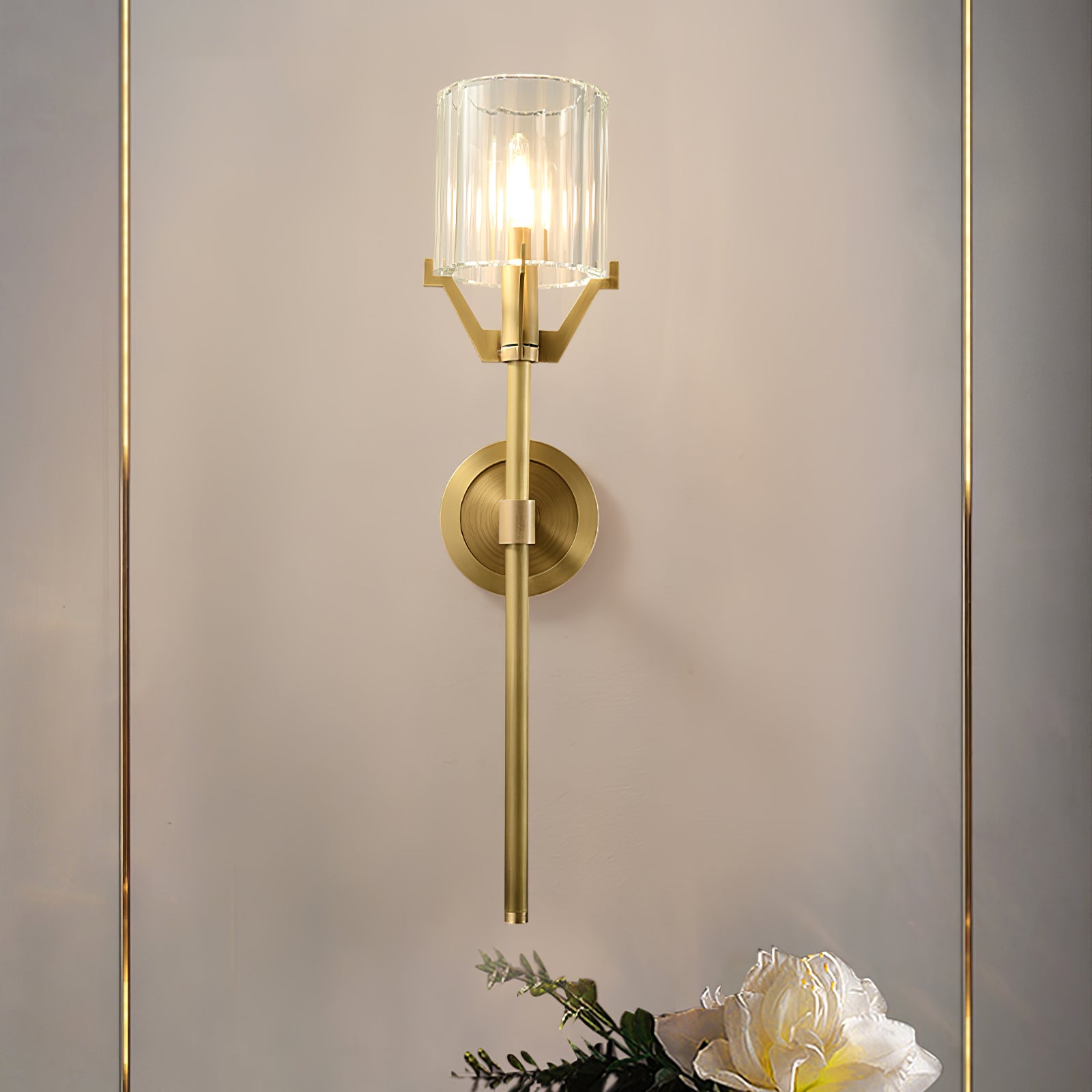 Lit brass wall lamp between thin gold-tone wall trims above white flowers