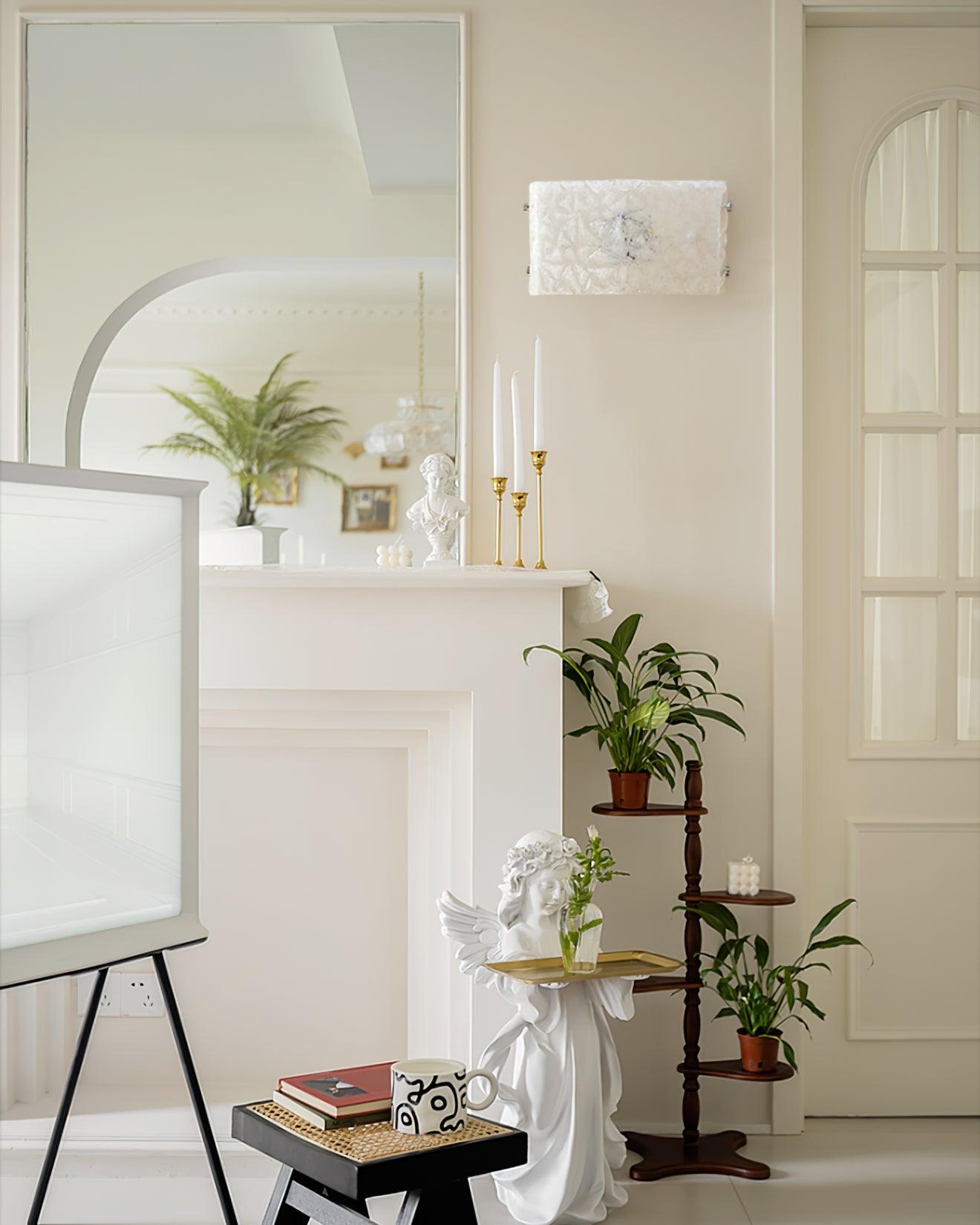 Unlit glass wall light above a white mantel with mirror, candles, bust, greenery and a winged sculpture below