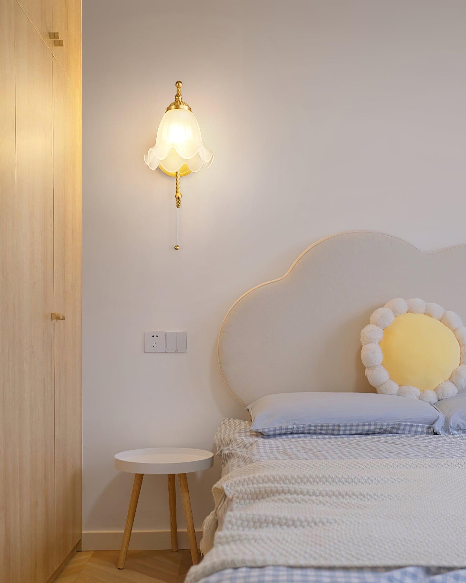 Front lit glass wall lamp beside white outlined bedhead with flower cushion, wooden wardrobe and small round bedside stool