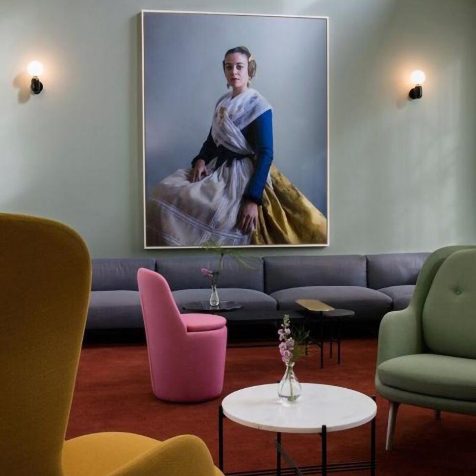 Two black globe wall lights flanking a large portrait above gray lounge seating, with pink, yellow and green chairs