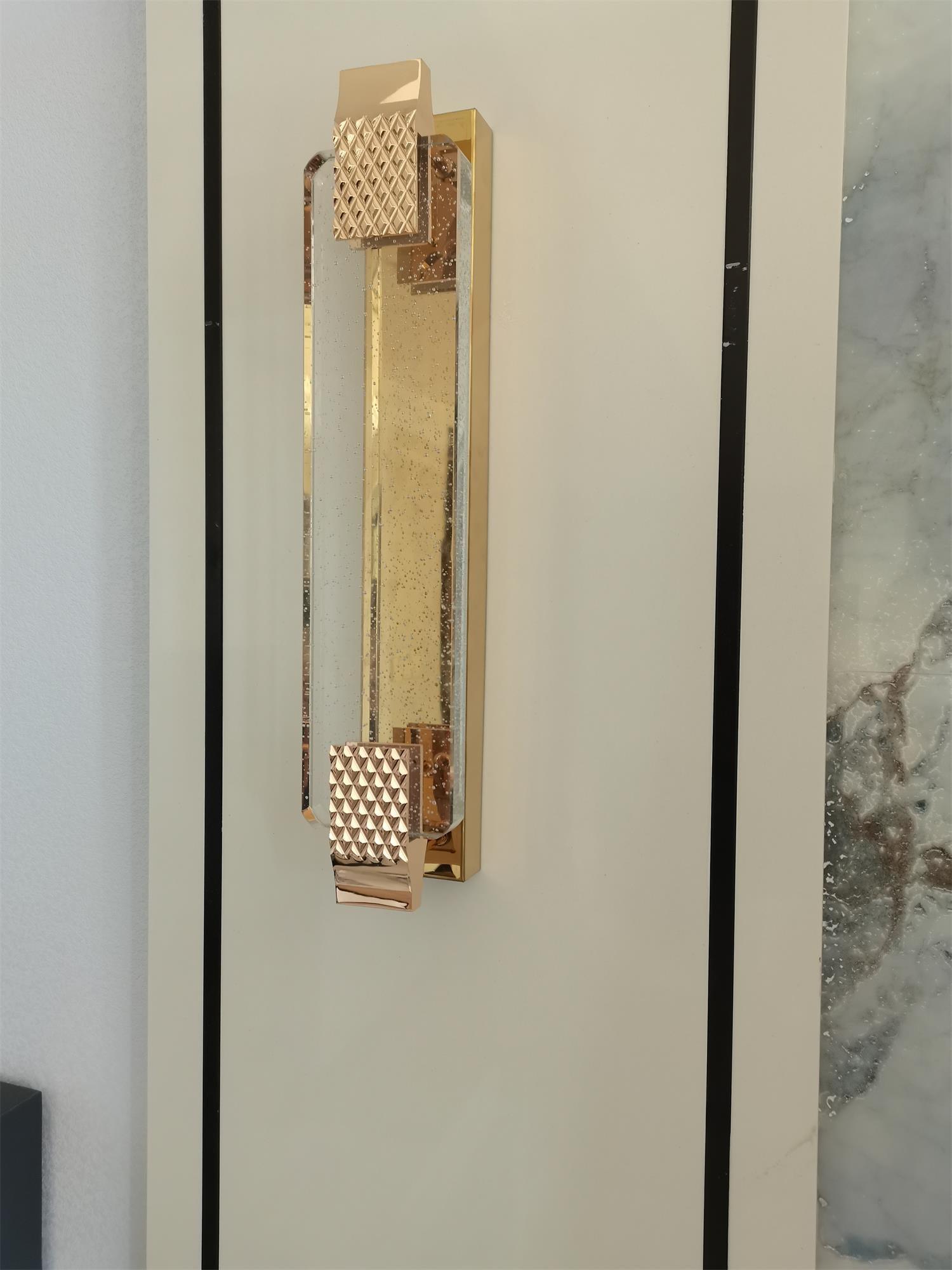 Unlit Moet wall light between dark vertical wall strips, showing its transparent bubble panel and rose gold metal straps