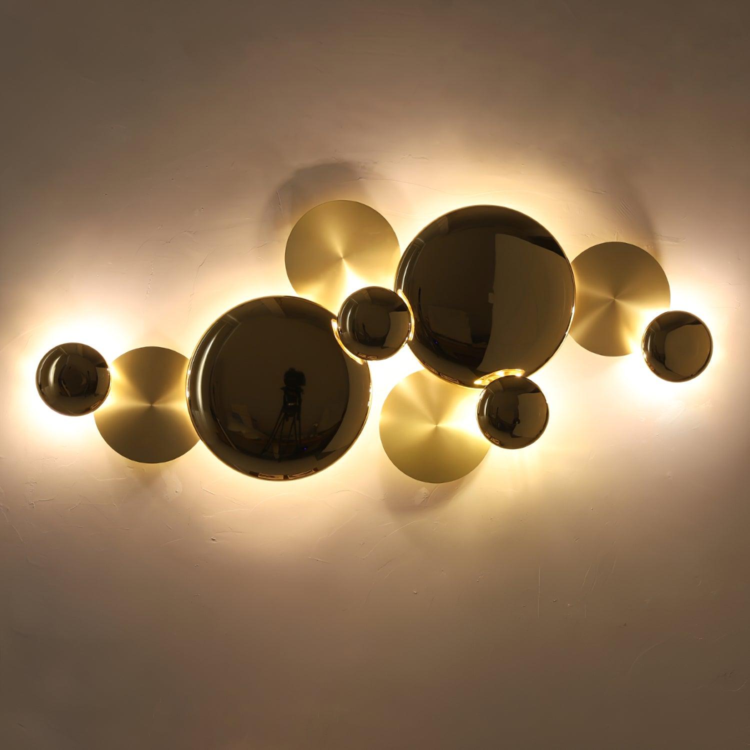 Gold disc wall lamp glowing in a darker room, with bright light outlining the reflective faces