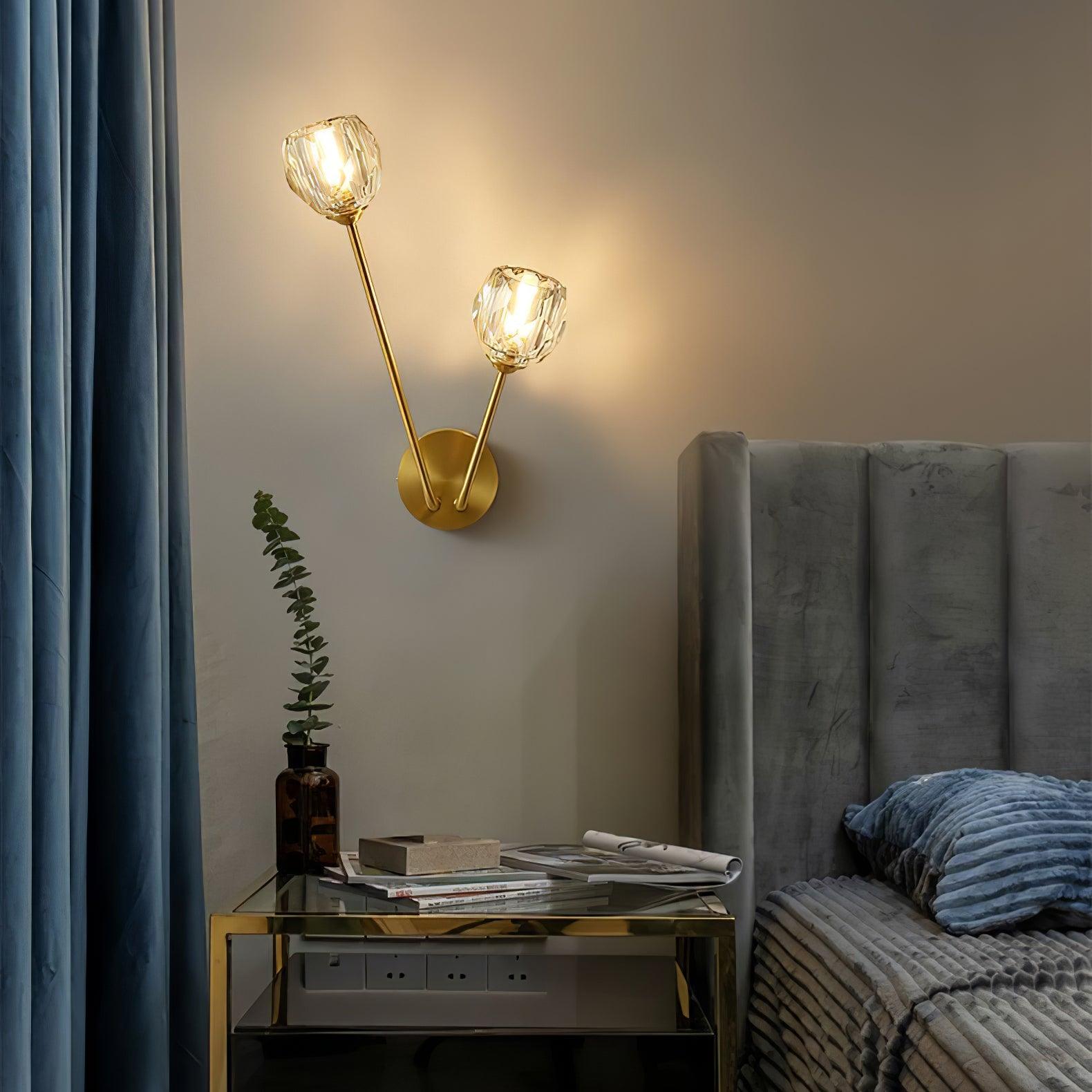Clear glass wall light beside a grey bed and blue curtain, above a glass-topped cabinet with a vase