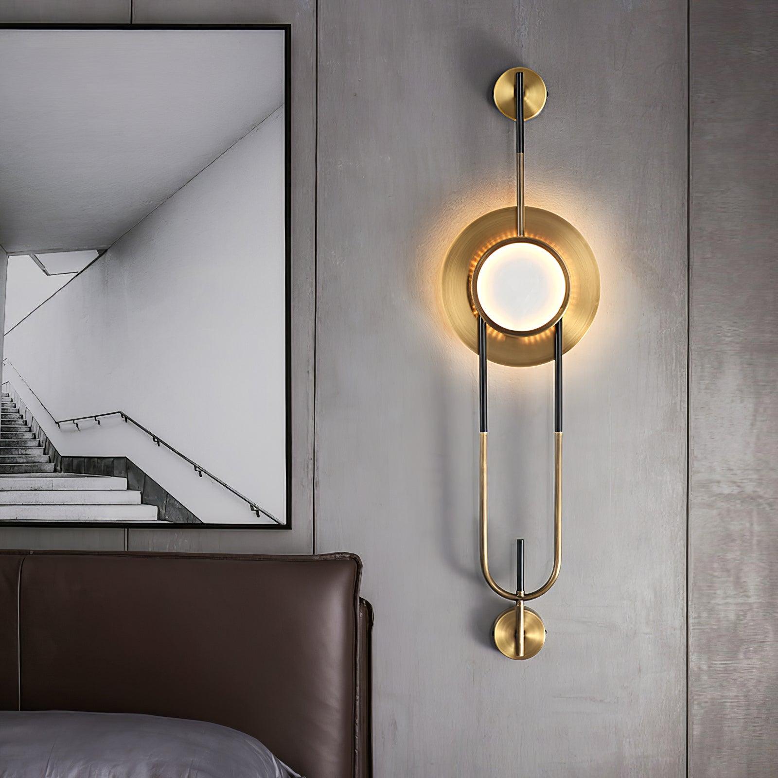 Glowing circular marble wall light beside a brown bed headboard and framed stair print