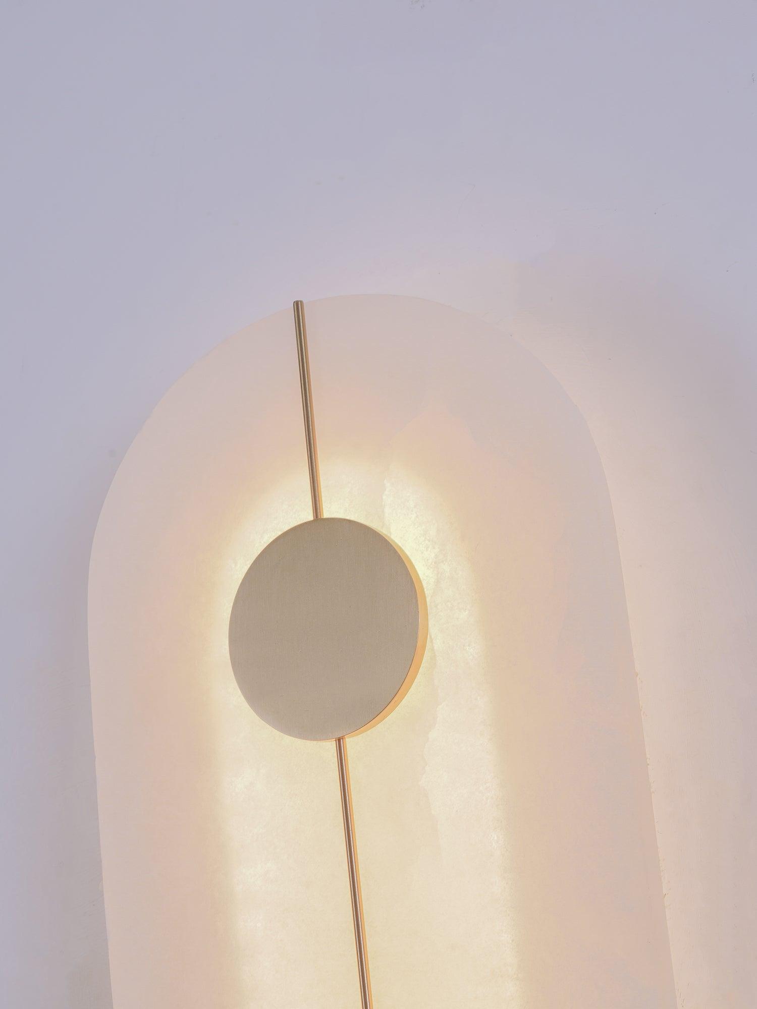 Upper end of an illuminated capsule wall light with a circular decorative disc