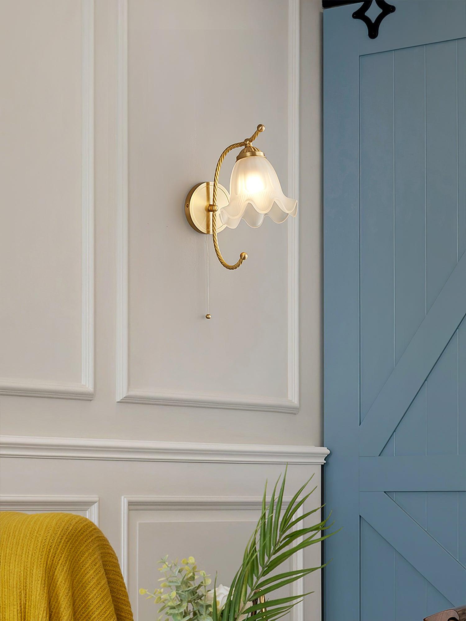 Opposite-side view of lit scalloped glass lamp beside blue sliding door and white wall moulding, with yellow throw below