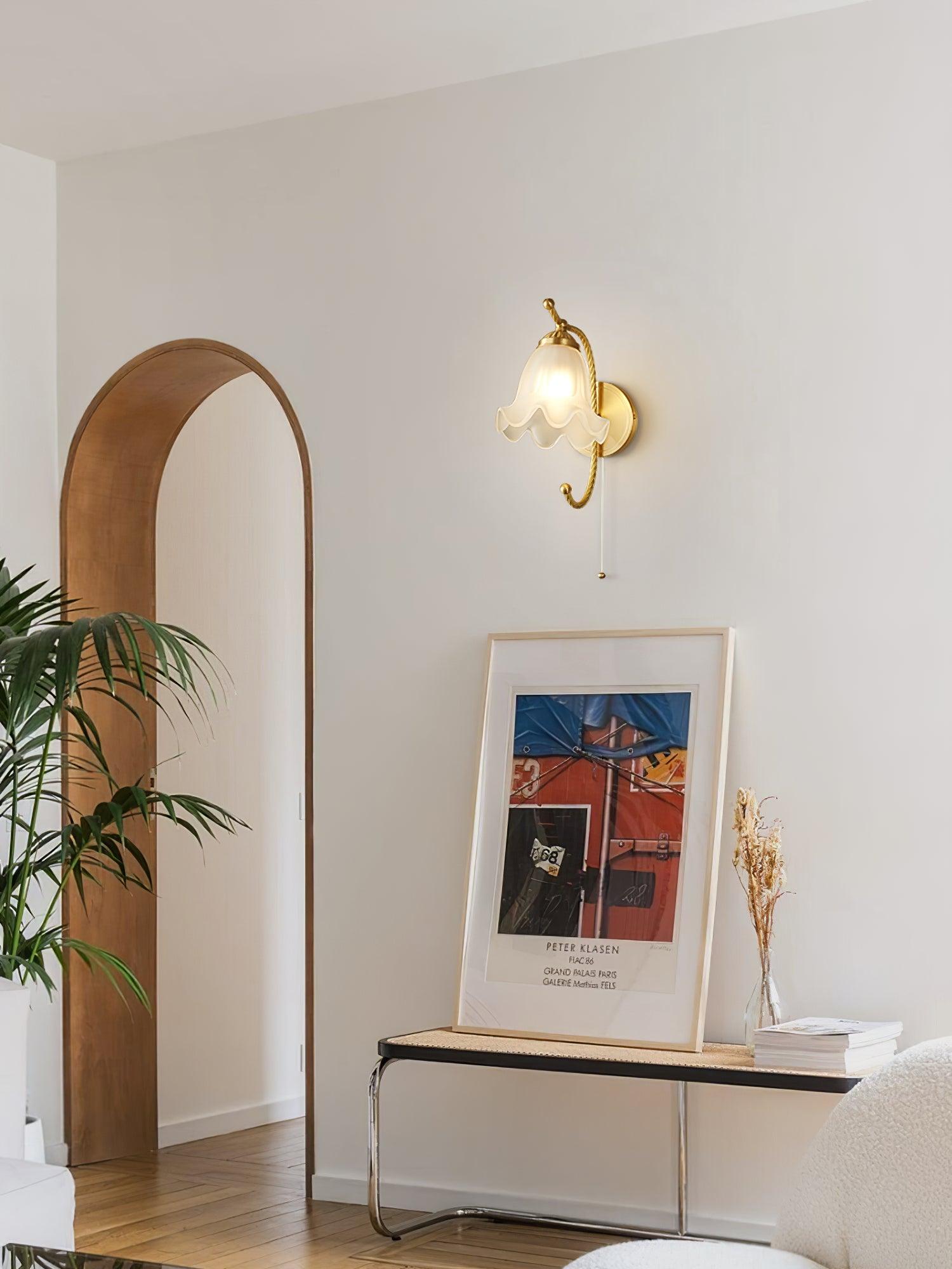 Single lit brass gooseneck lamp above console with framed art and vase, beside a tall wood-framed arched mirror