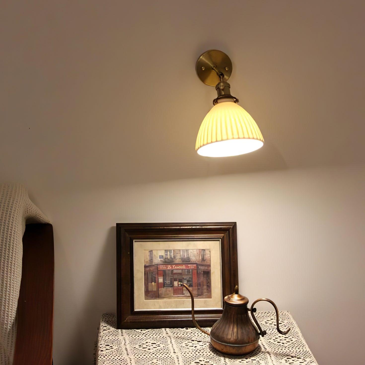 Wide view of a pleated ceramic wall lamp above a framed picture and metal pot beside upholstered furniture