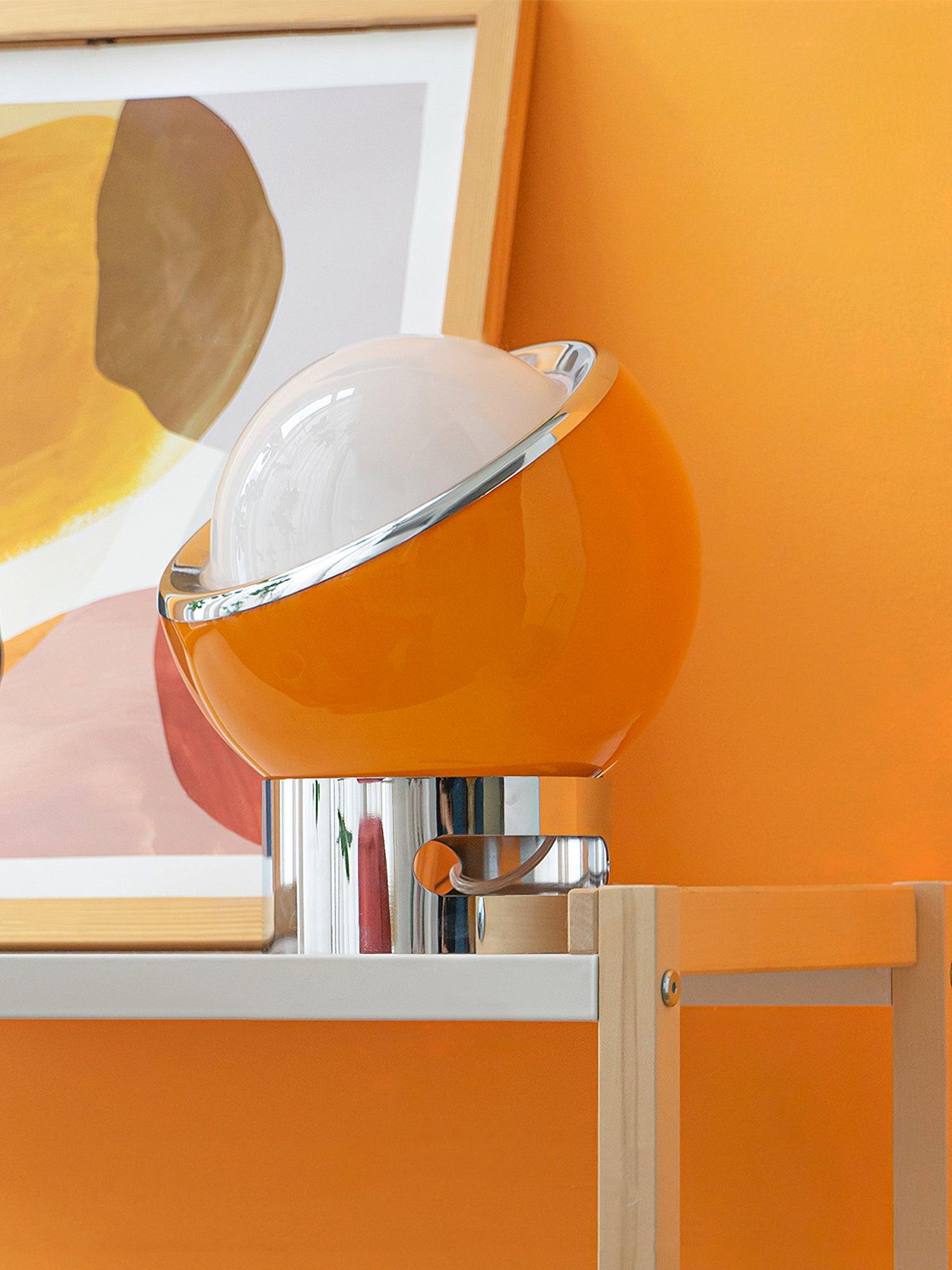 Orange-toned Valeria glass shade and chrome base beside framed art