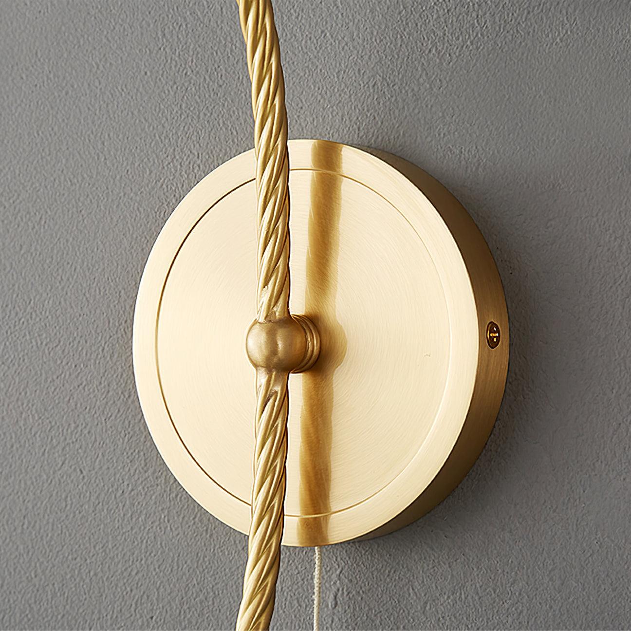 Close-up of round brass-finish wallplate, edge screw, central collar and rope-textured stem, with pull cord below