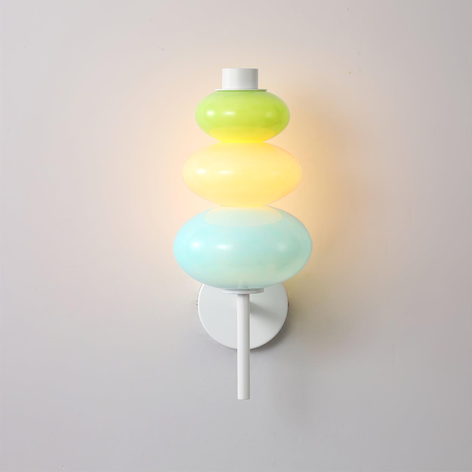Front view of the lit multicolored glass stack on a pale wall, with a white pole extending below