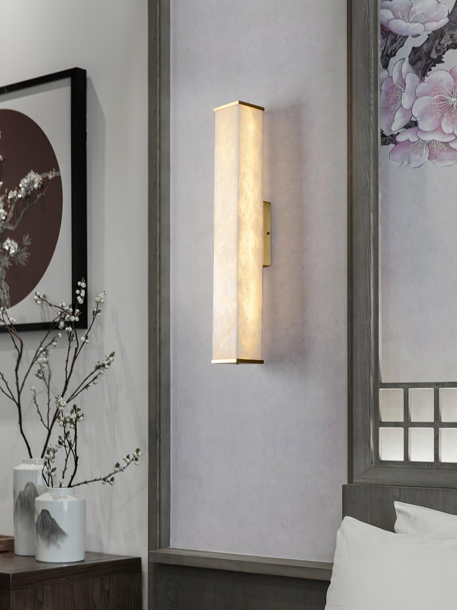 Alabaster wall light on a bedroom wall panel between red-circle artwork and mirrored trim, above white bedding and branch vases