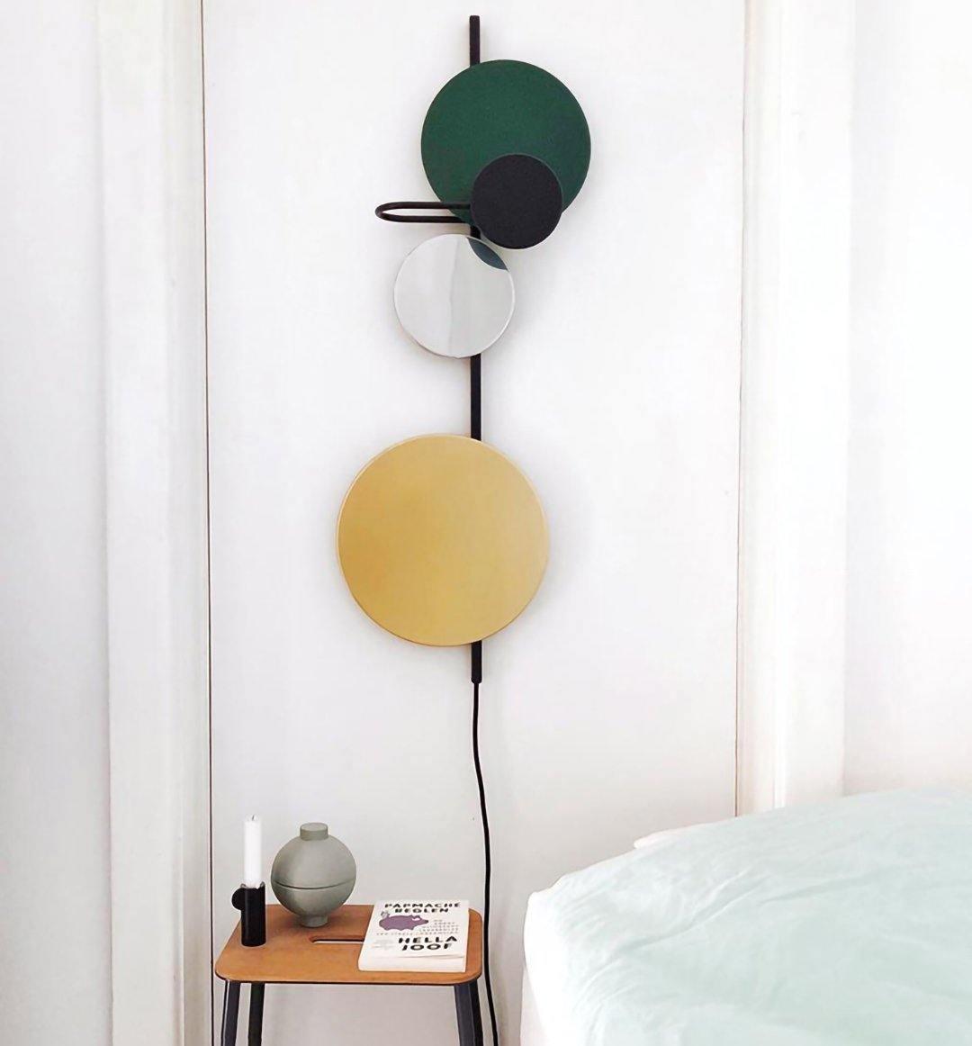 Green disc wall lamp beside a bed