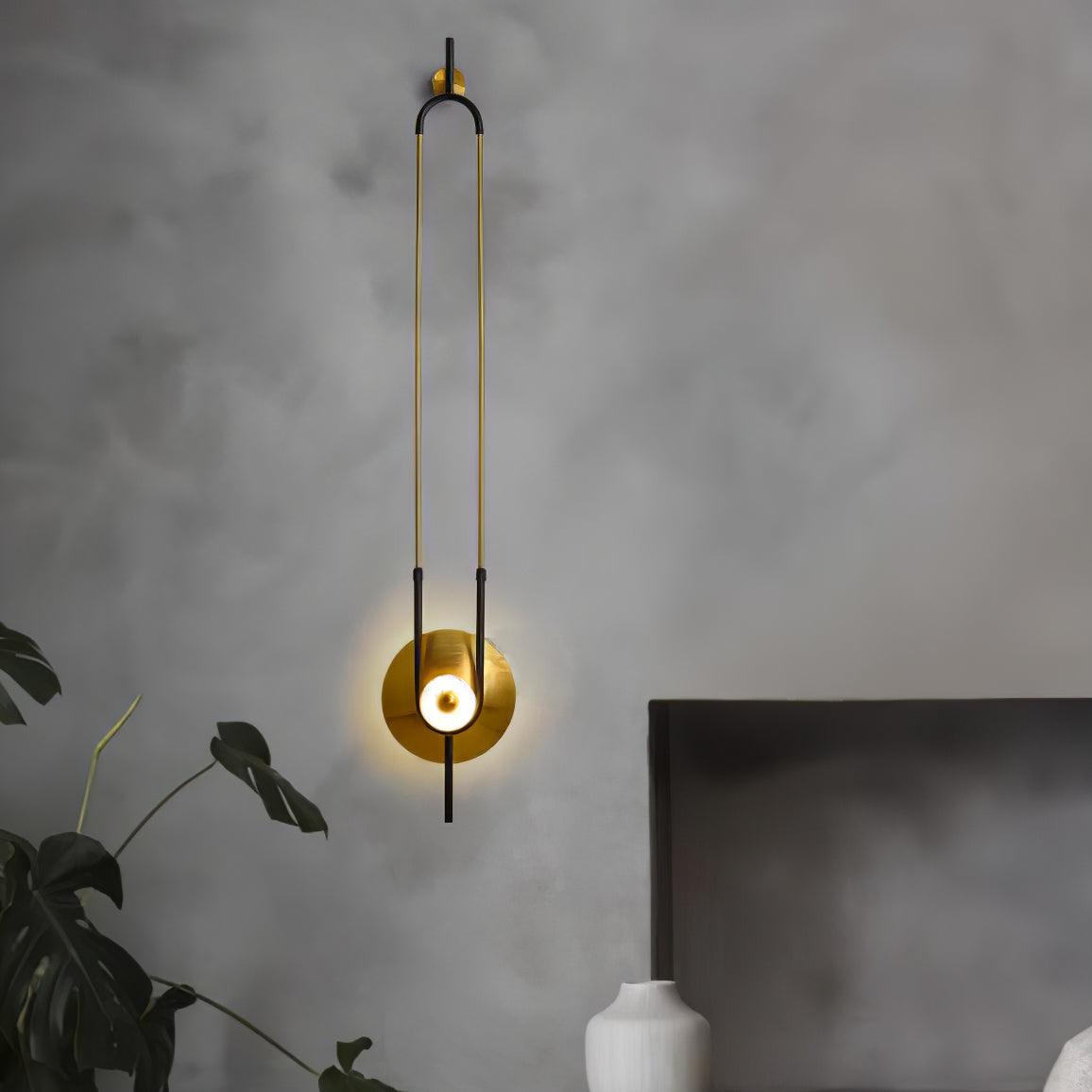 Lit elongated loop wall light beside dark headboard, white ribbed vase and large green leaves on a grey wall