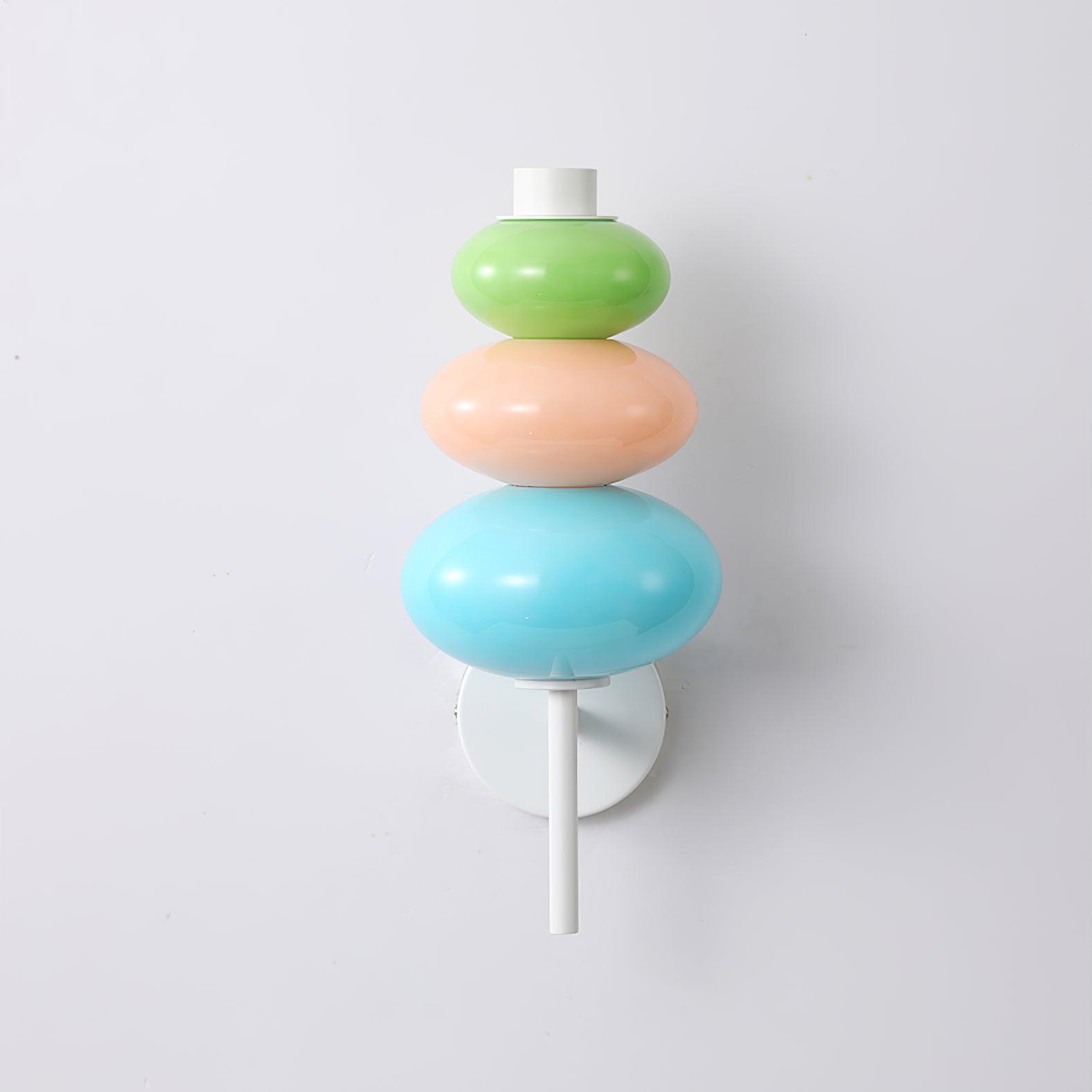 Unlit green, peach-pink and blue glass segments stacked above the white pole and round wall plate