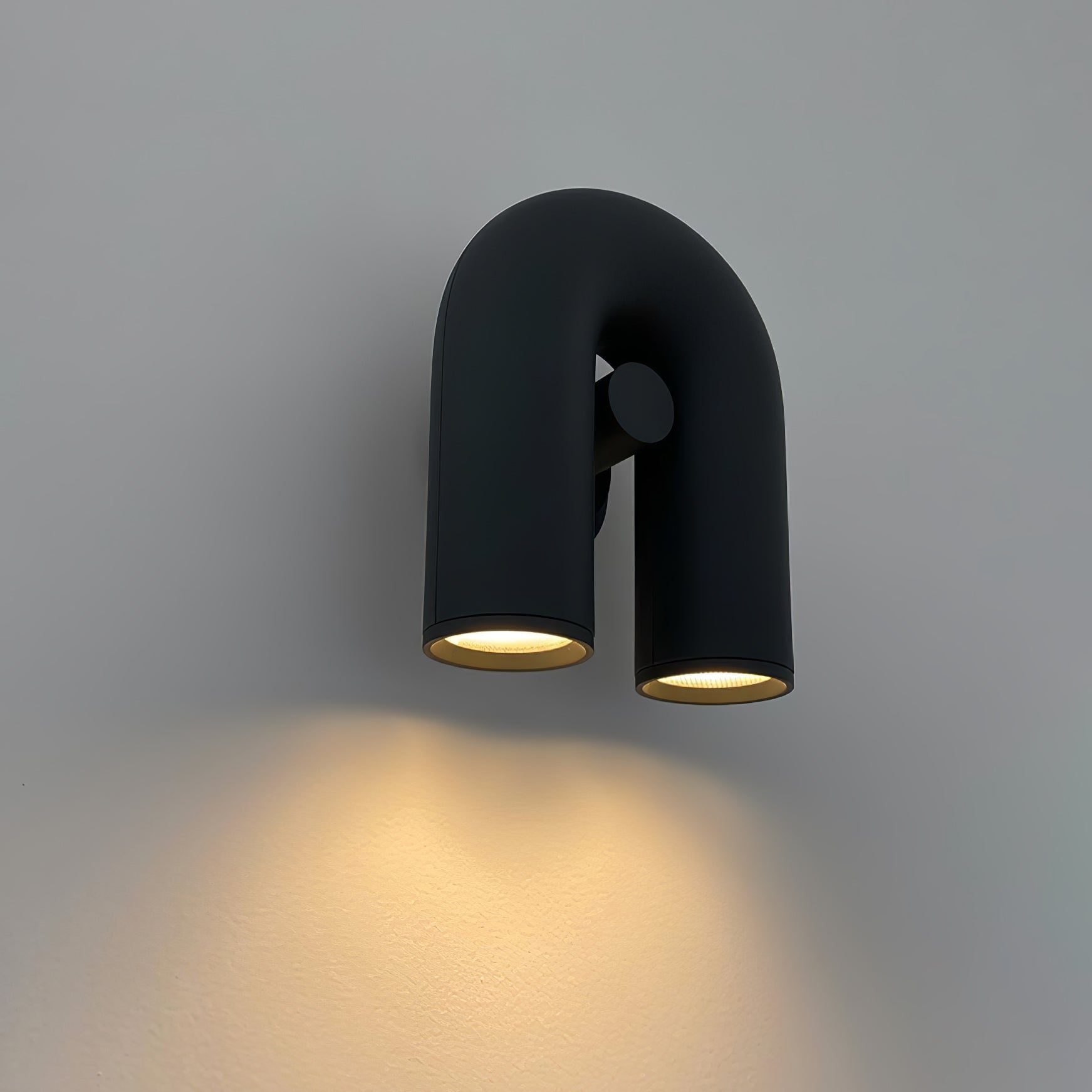 Black Cirkus wall lamp angled against a grey wall with light shining downwards