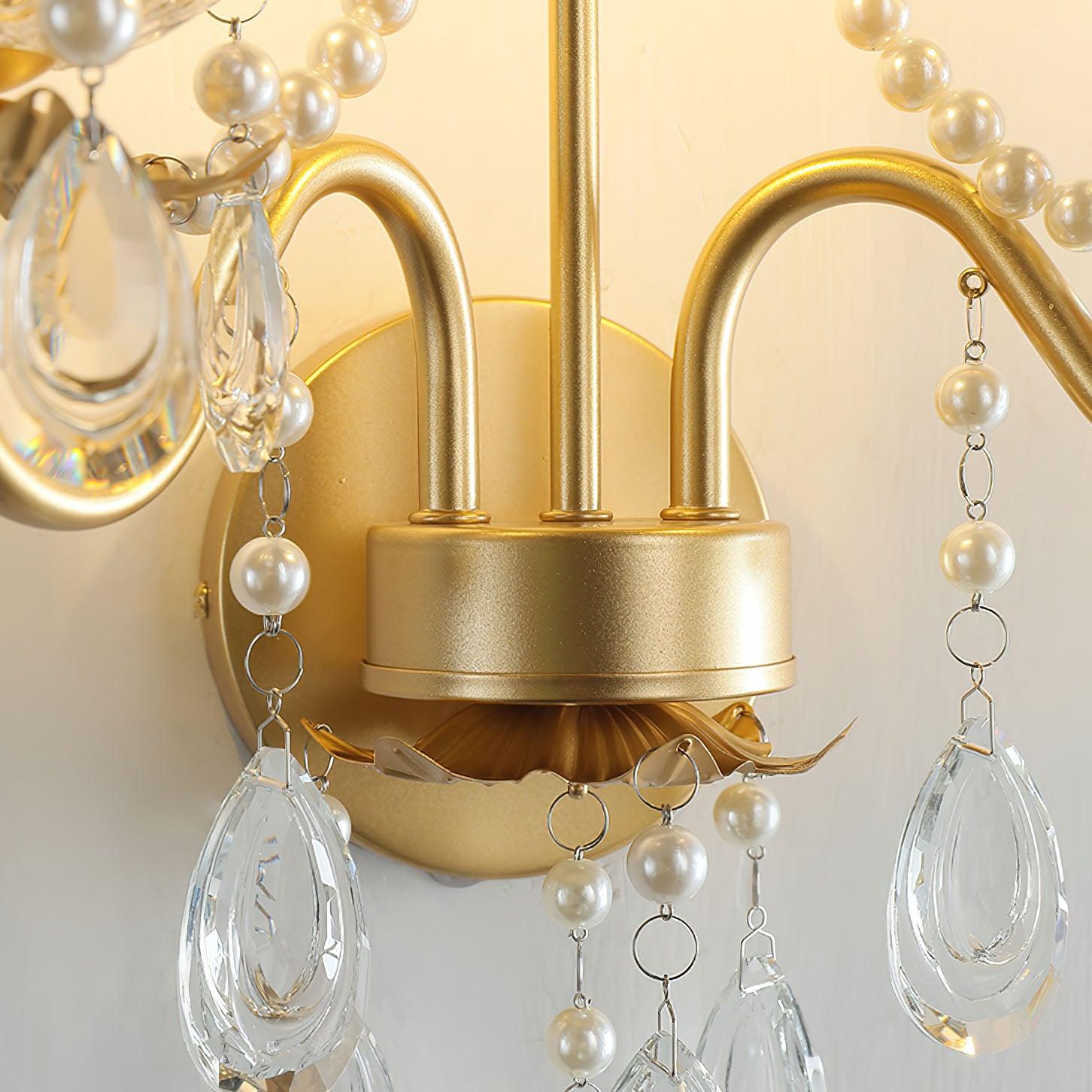 Lit detail of gold central hub and round plate, curled arms, scalloped lower support, bead chains and clear teardrop-shaped drops