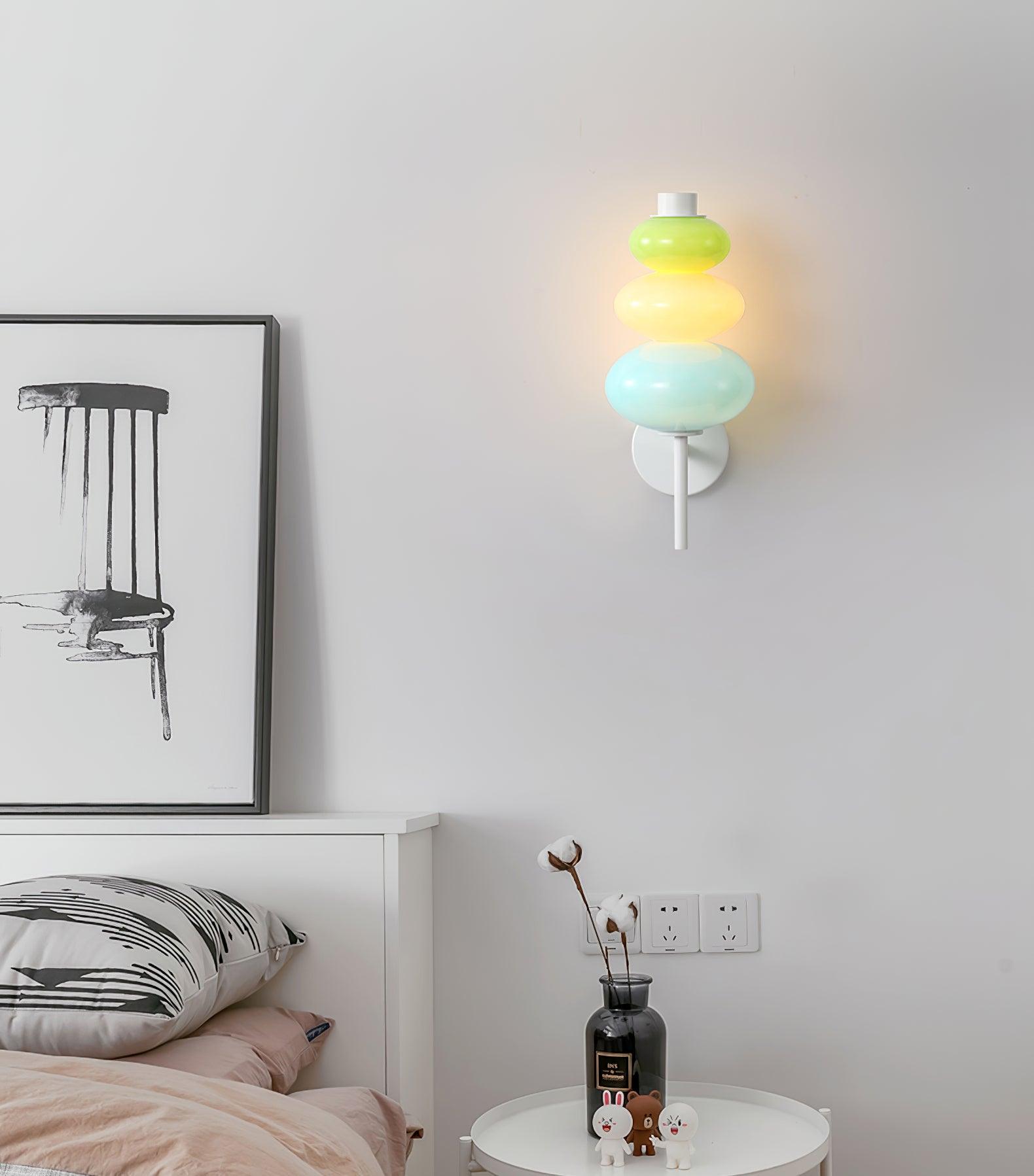 Colored glass wall light above a white bedside cabinet with a black vase and rabbit ornaments