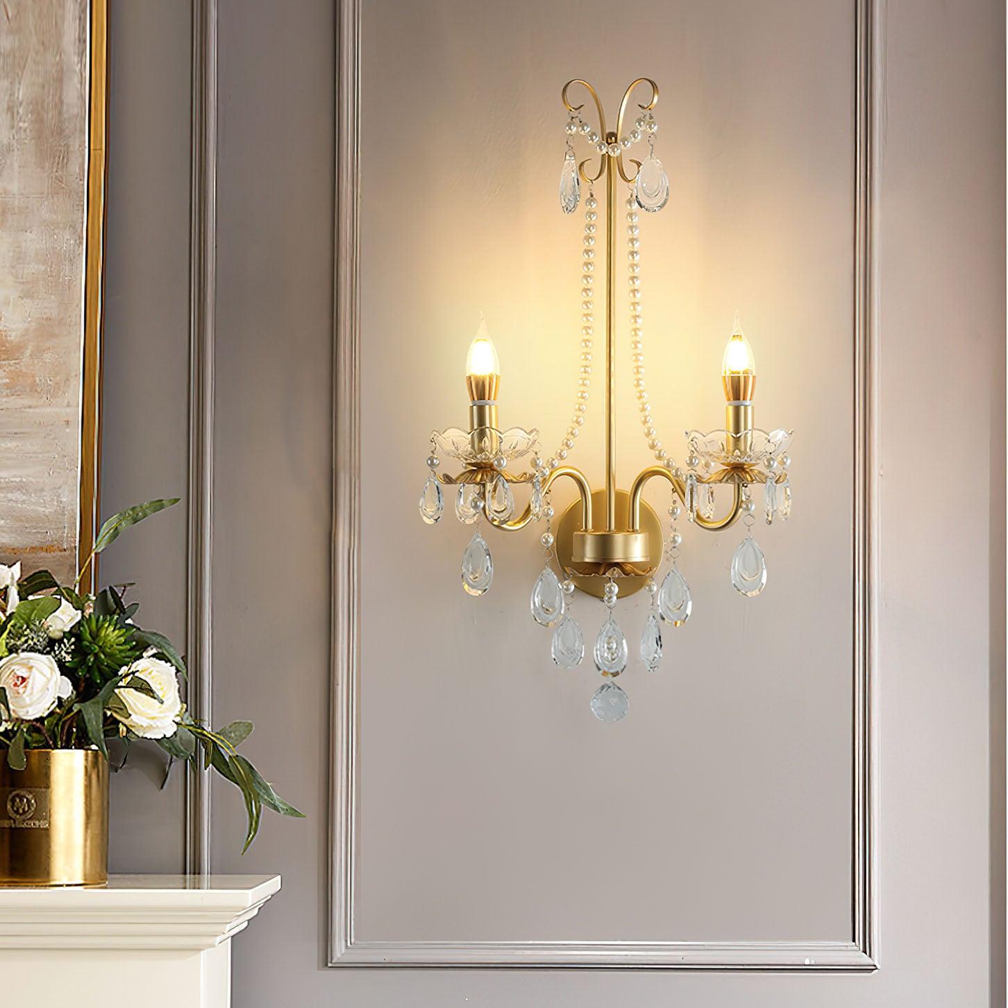 Glowing gold-finish wall light in silver-bordered grey panel beside gold vase and white flowers on a white console