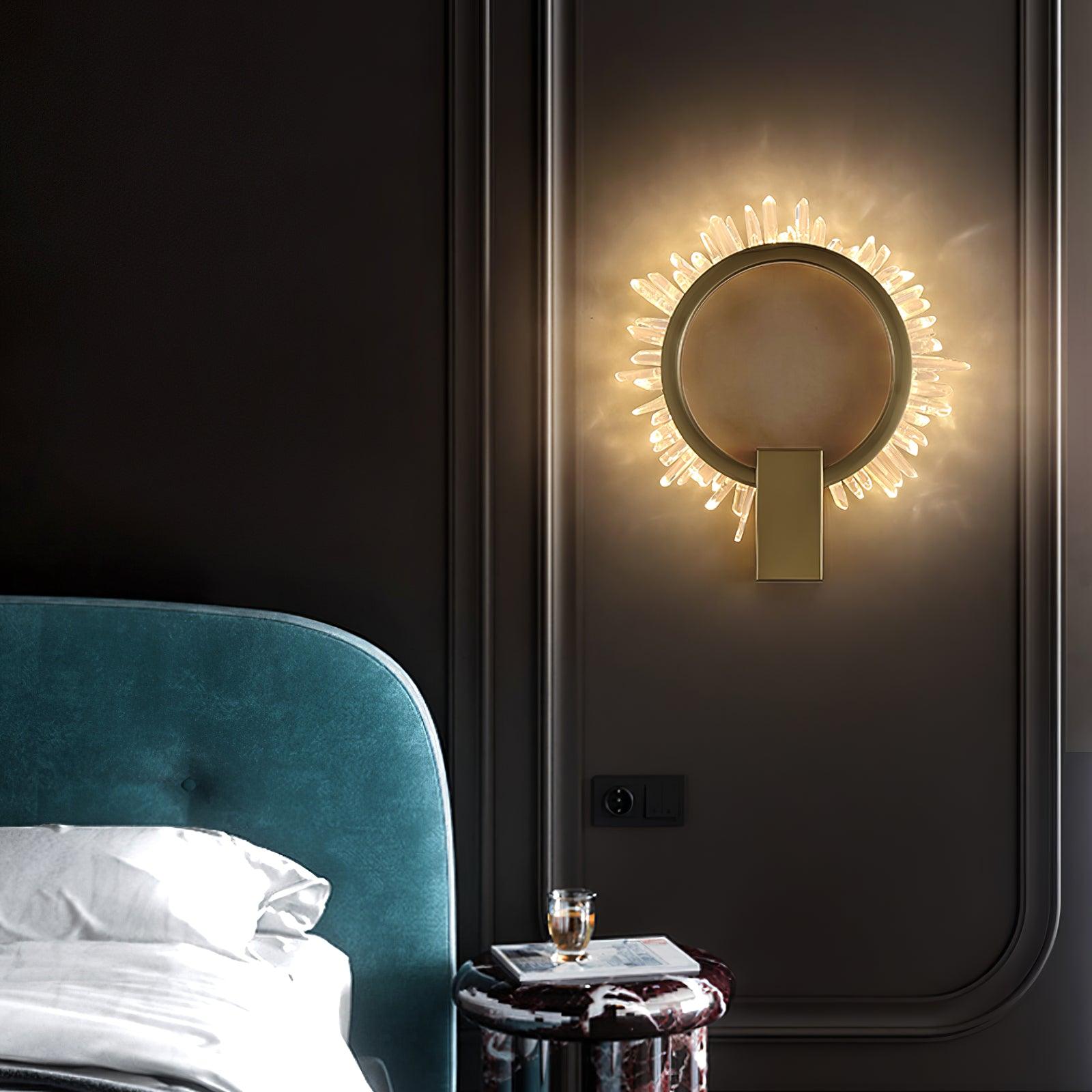 Lit crystal ring wall lamp beside a teal upholstered bedhead and marble-look nightstand