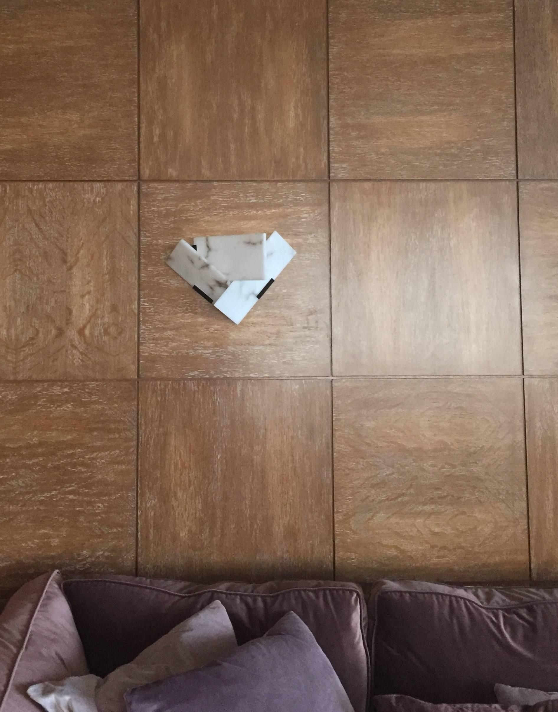 Farther unlit alabaster wall sconce on wood paneling above a sofa with purple-grey cushions