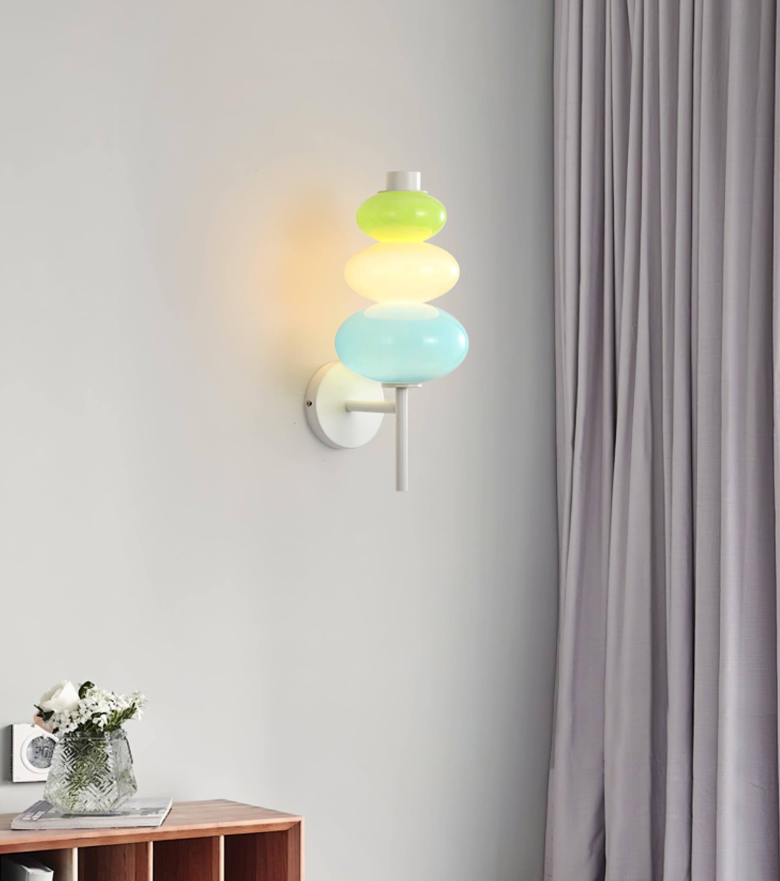 Lit glass wall fixture above a wooden cabinet with flowers and a camera beside curtains