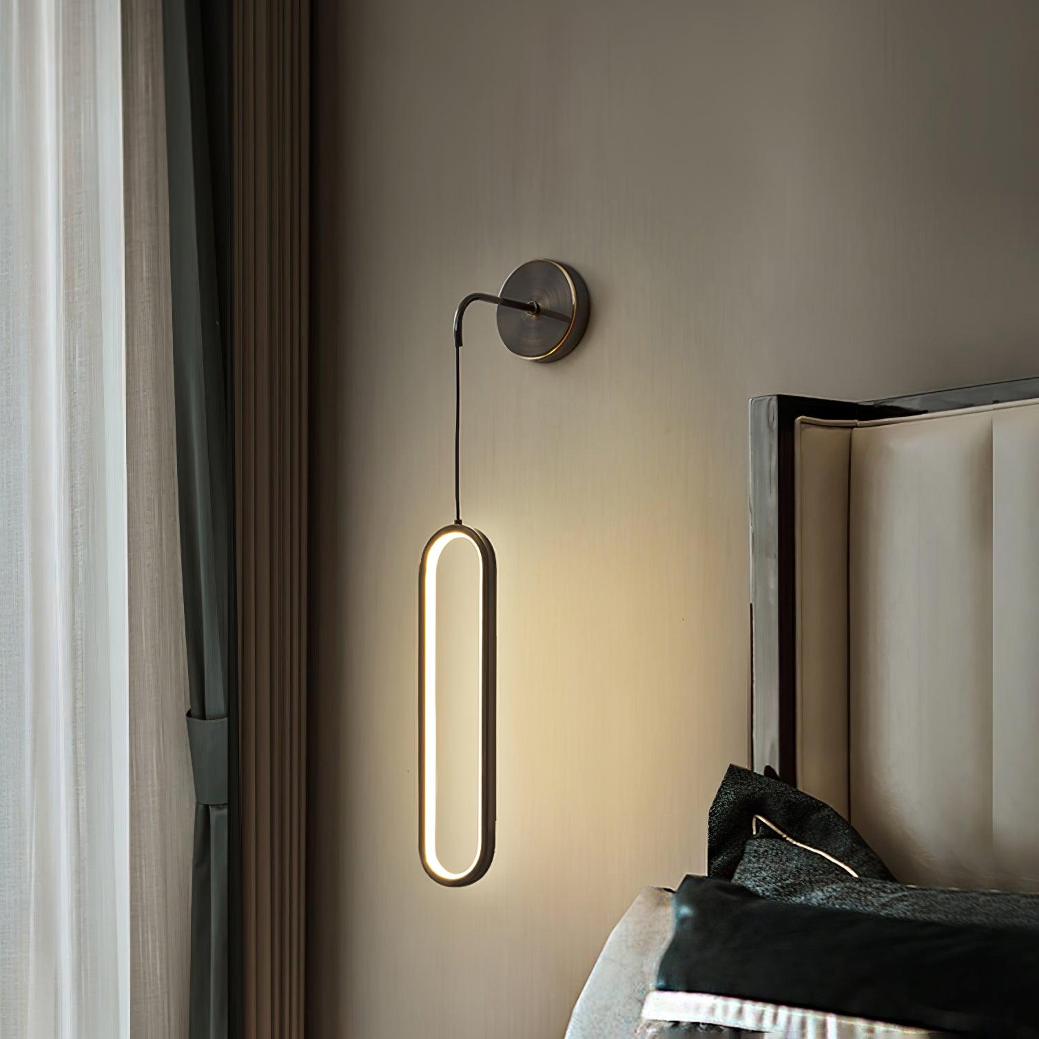 Illuminated oval ring below a dark wall plate beside a padded headboard and curtains