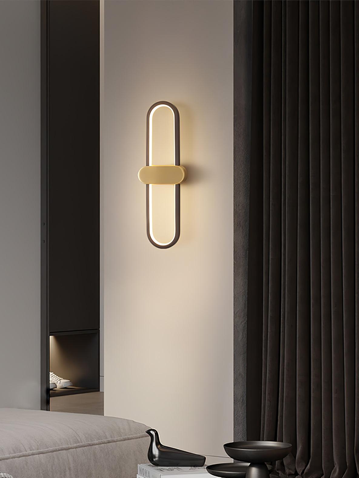 Black-loop wall lamp with gold-coloured centre above a grey bed edge and black decorative bowls