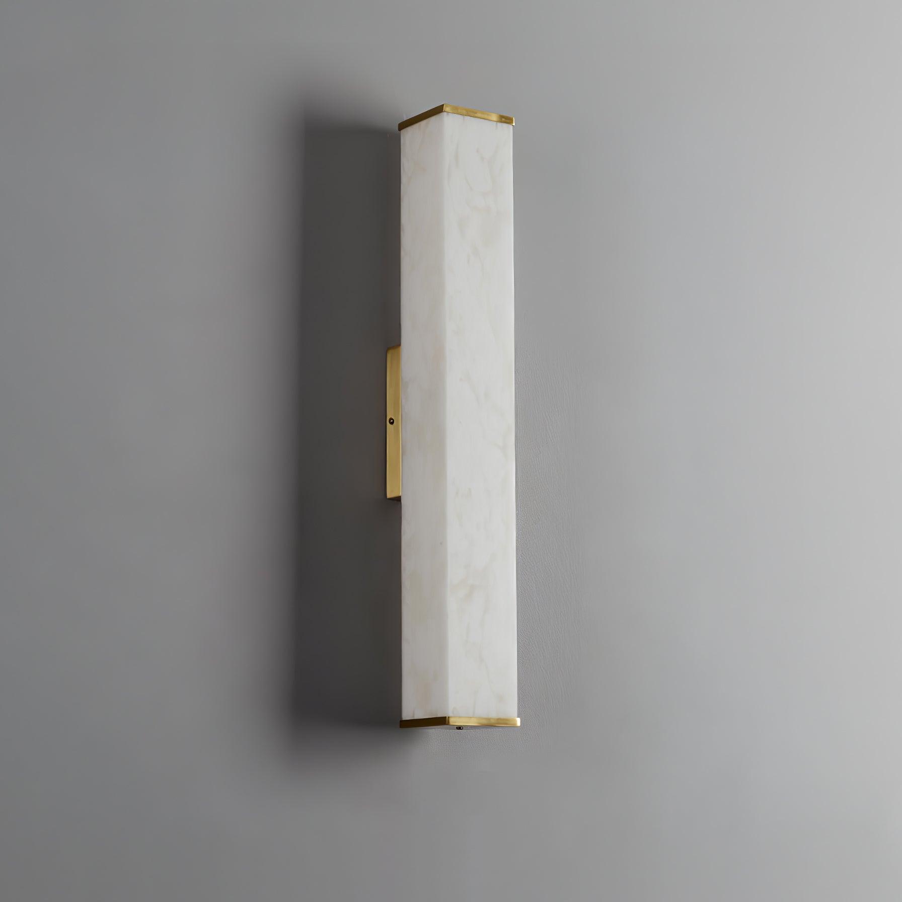 Unlit white veined alabaster wall light on a gray wall with brass top and bottom caps and a left-side mounting plate