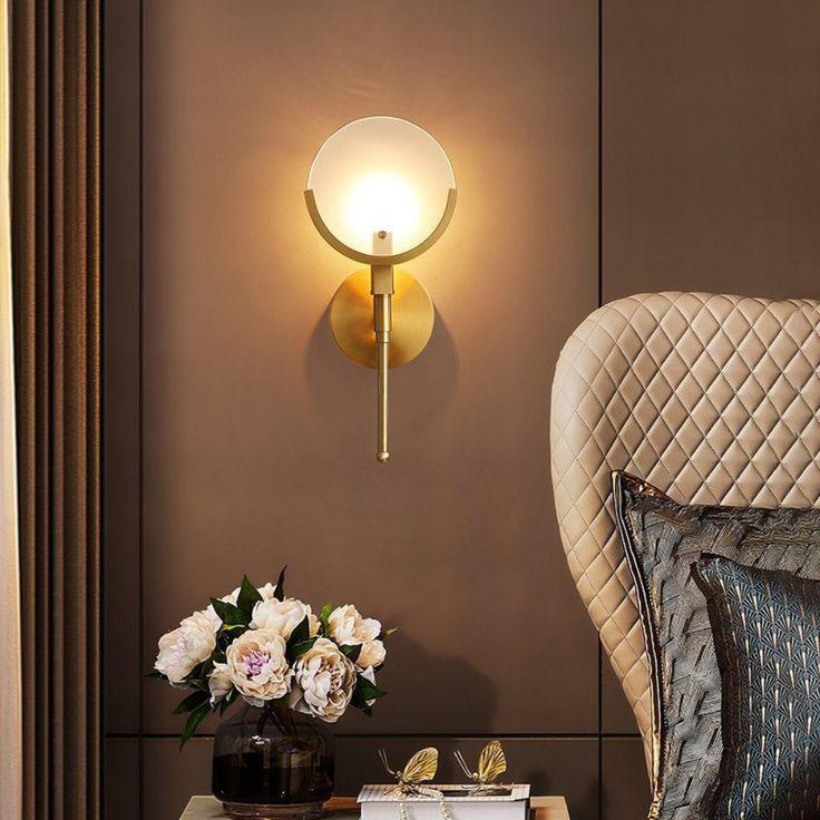 Lit short-stem Ava wall light beside a quilted headboard and curtain, above flowers and books