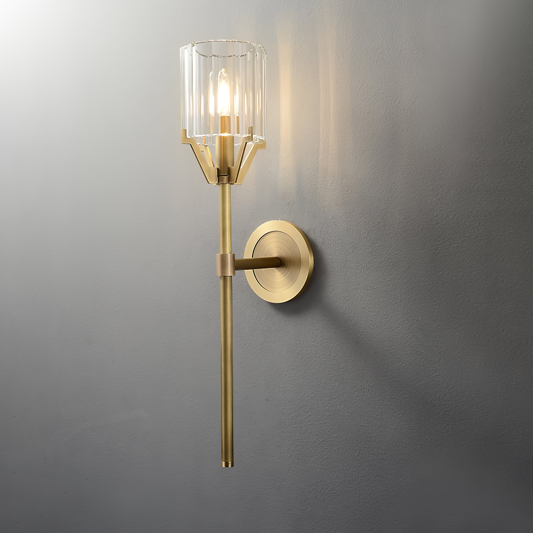 Lit angled wall lamp with a clear faceted shade, round backplate on the right and long straight brass stem