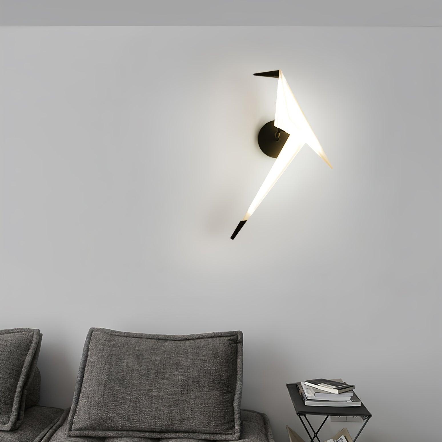 Black and White bird wall light glowing above a gray sofa beside a small table with books
