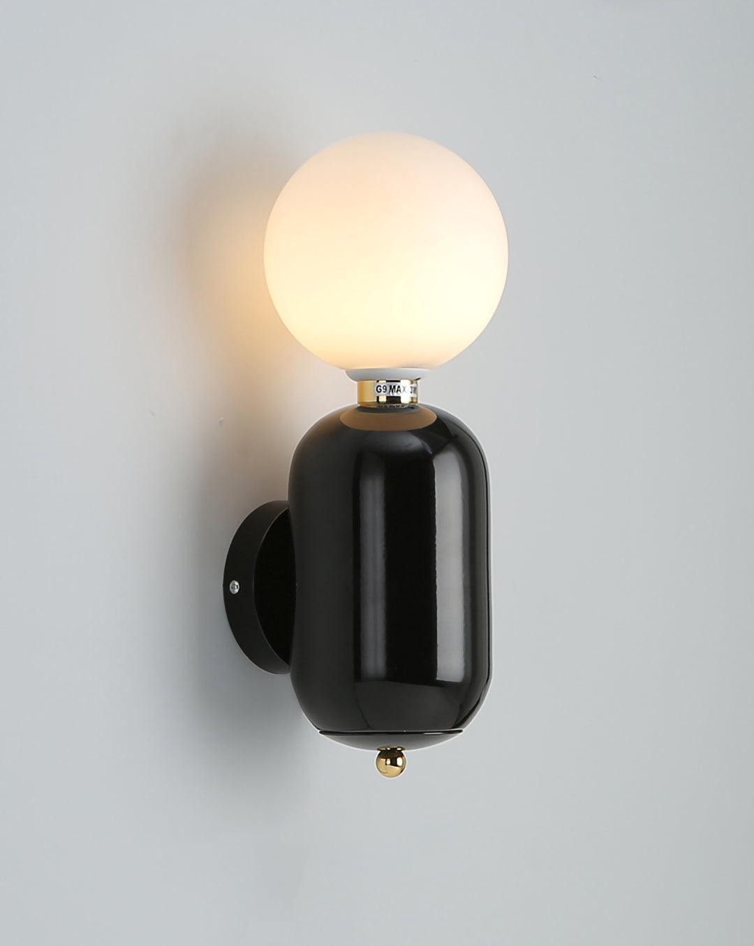 Black Aballs wall sconce lit on gray wall, white globe above glossy body, black round plate and gold-tone lower ball