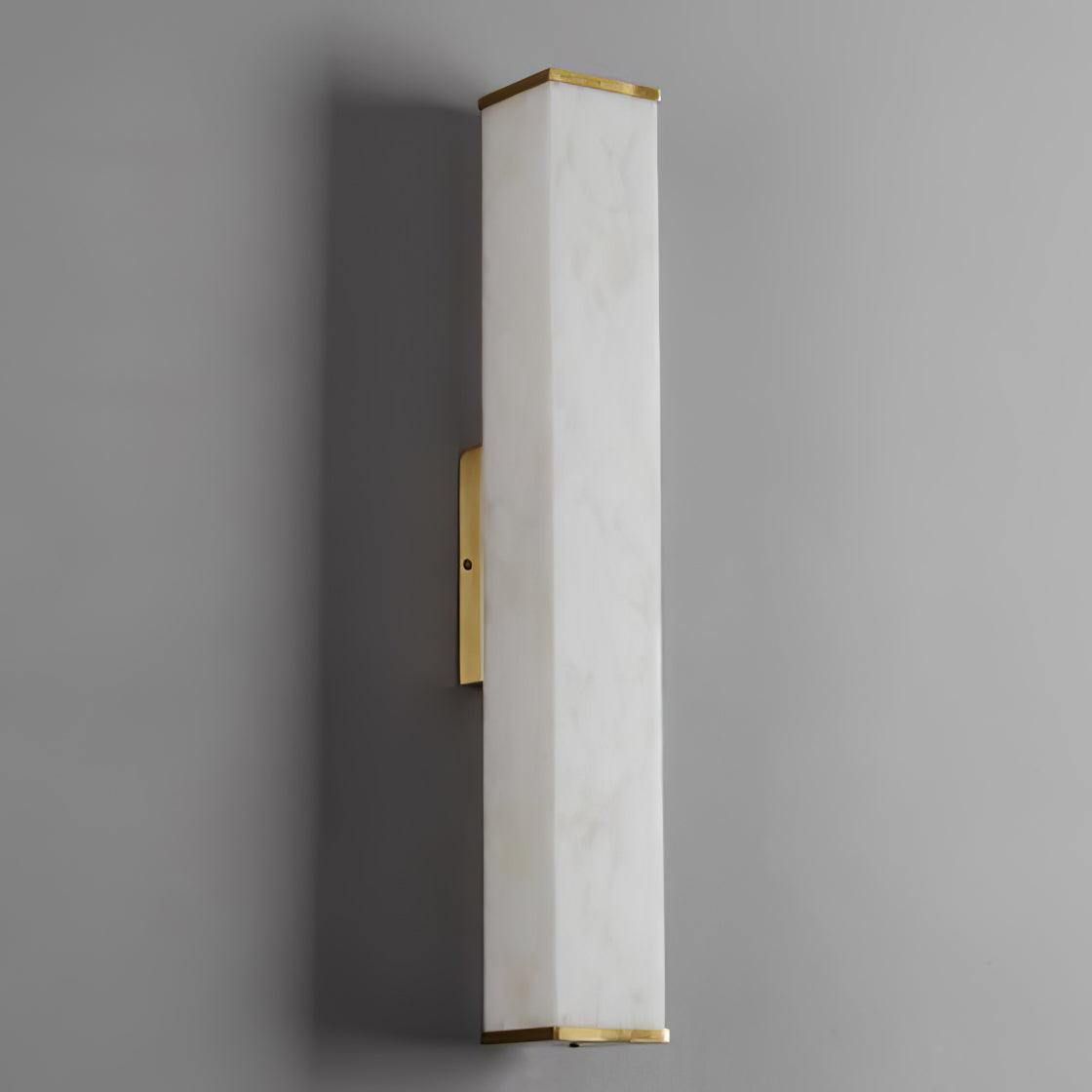 Tall unlit alabaster wall light with faint natural veining, thin brass end caps and a narrow plate against a gray wall