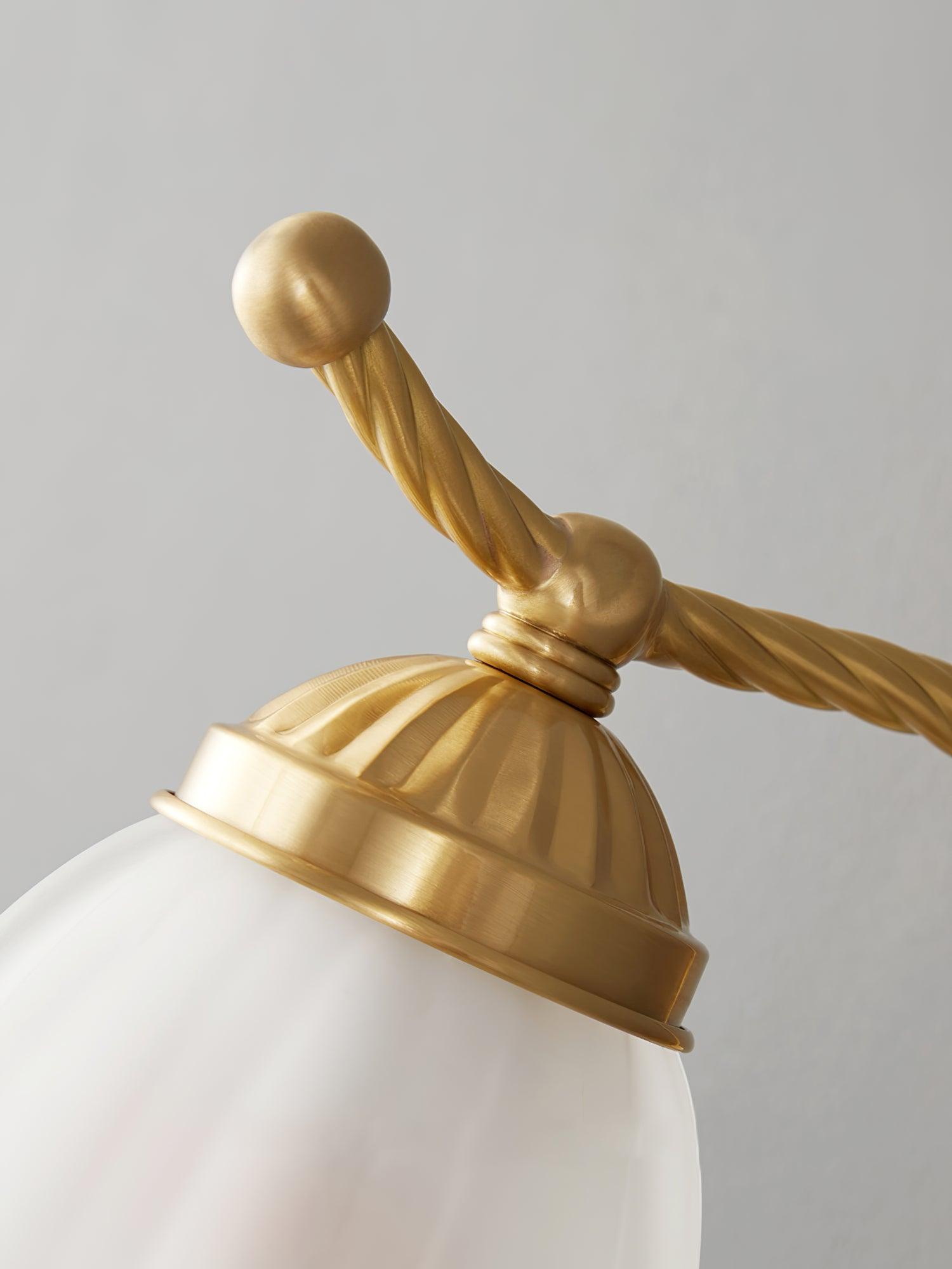 Detail of brass-finish ribbed shade cap, round top finial and twisted curved arm above opaque glass shade