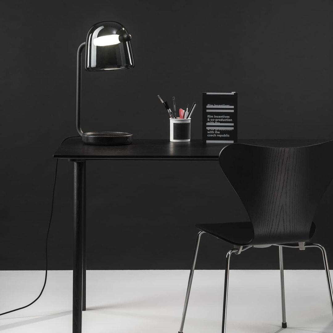 Black Mona lamp on a dark desk beside stationery
