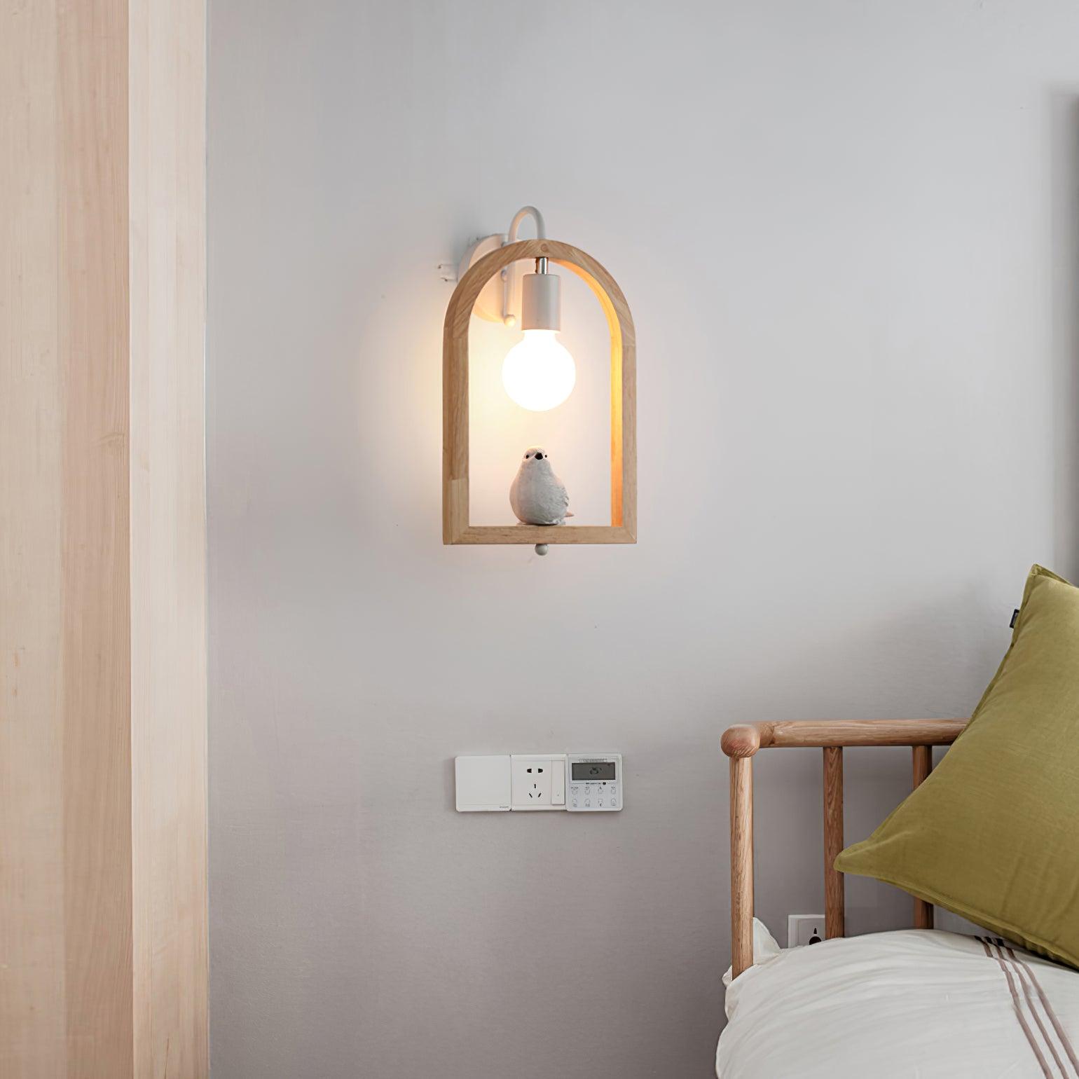 Bird wall light beside a wooden bed with a green cushion, with an exposed glowing bulb and wall socket panel below