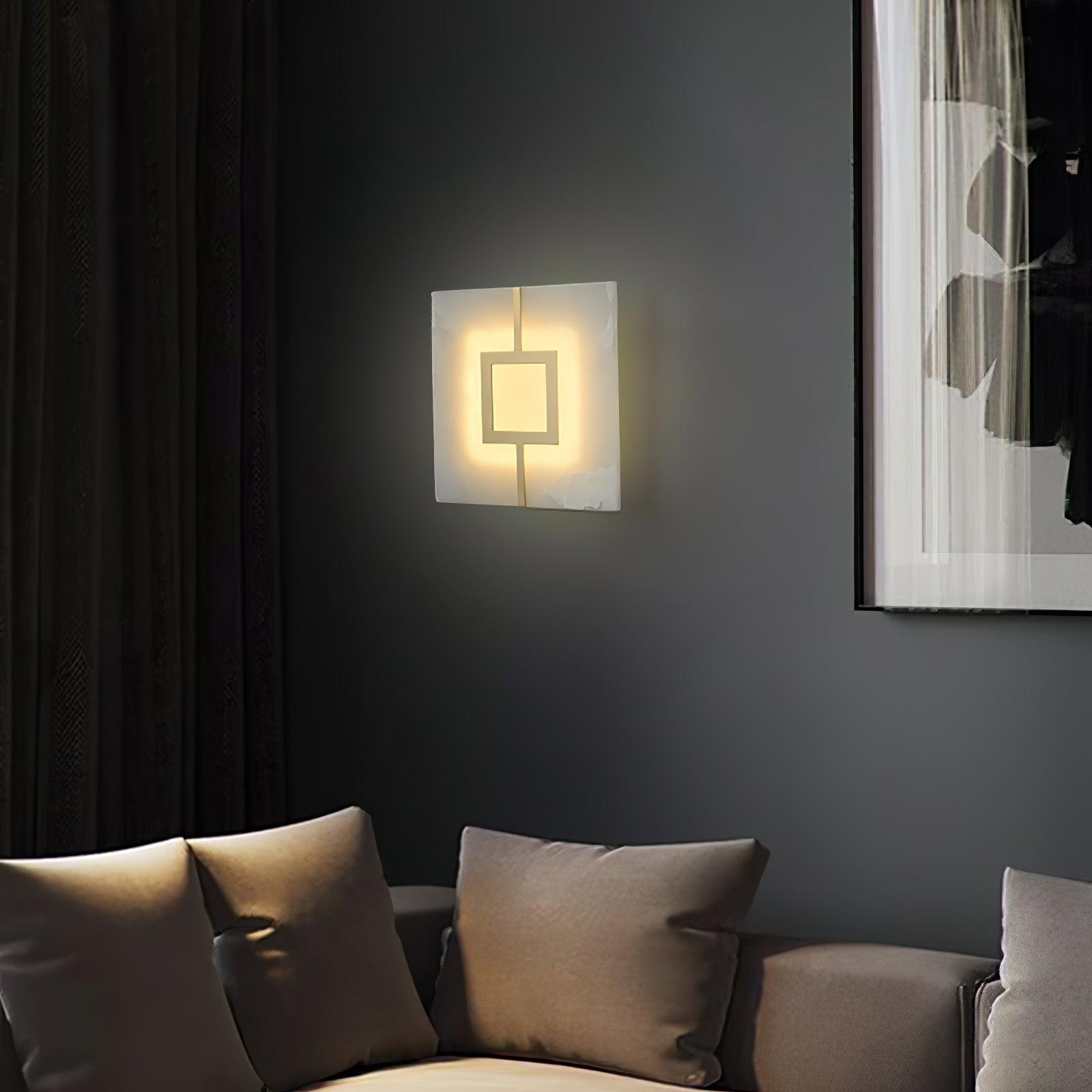 Lit square veined wall light with one open brass-tone square above a grey sofa beside framed art and curtains