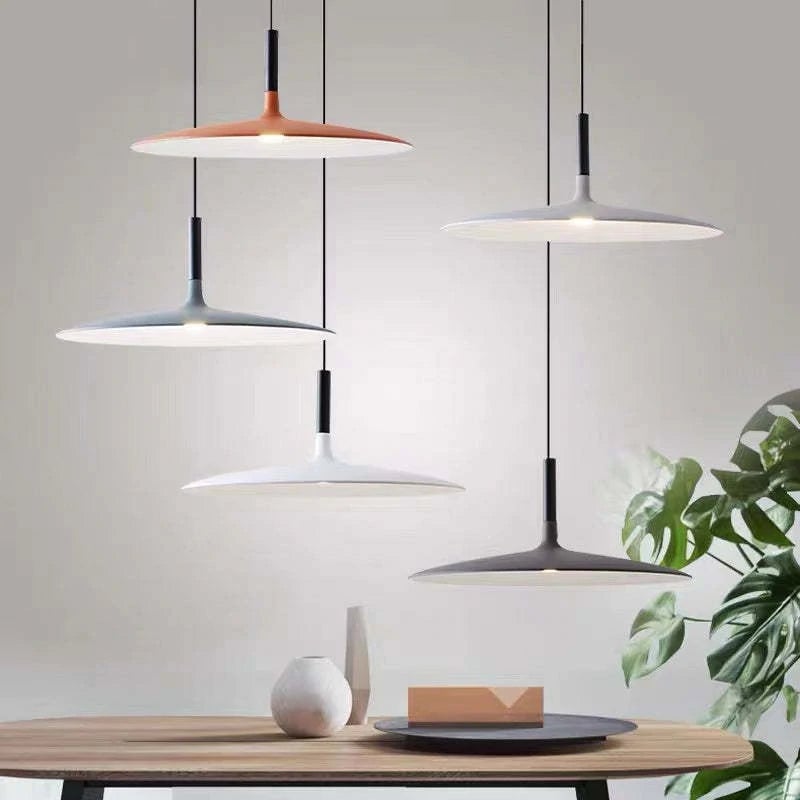 Five assorted shallow dome pendants at staggered heights above a wooden table near a plant