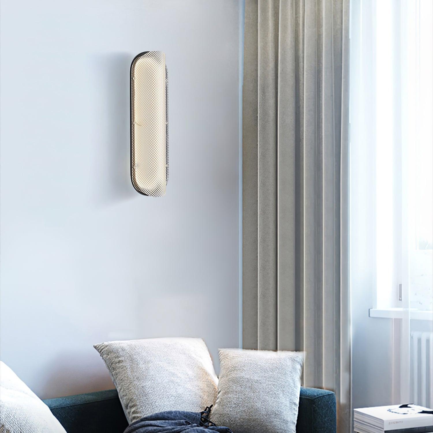 Angled lit textured glass wall light above a teal sofa with pale cushions beside a curtained window