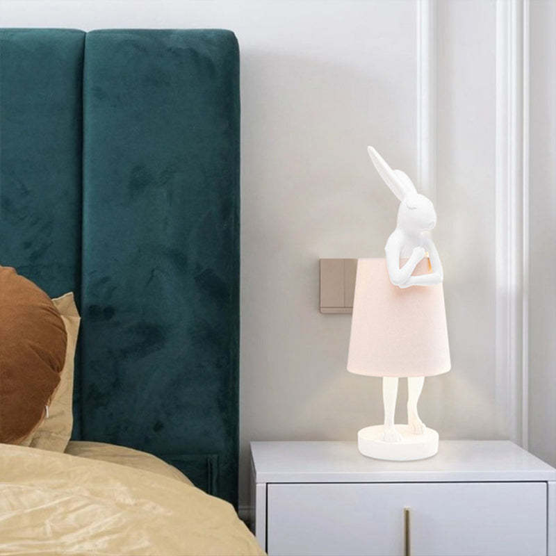 White rabbit table lamp beside a teal upholstered bed