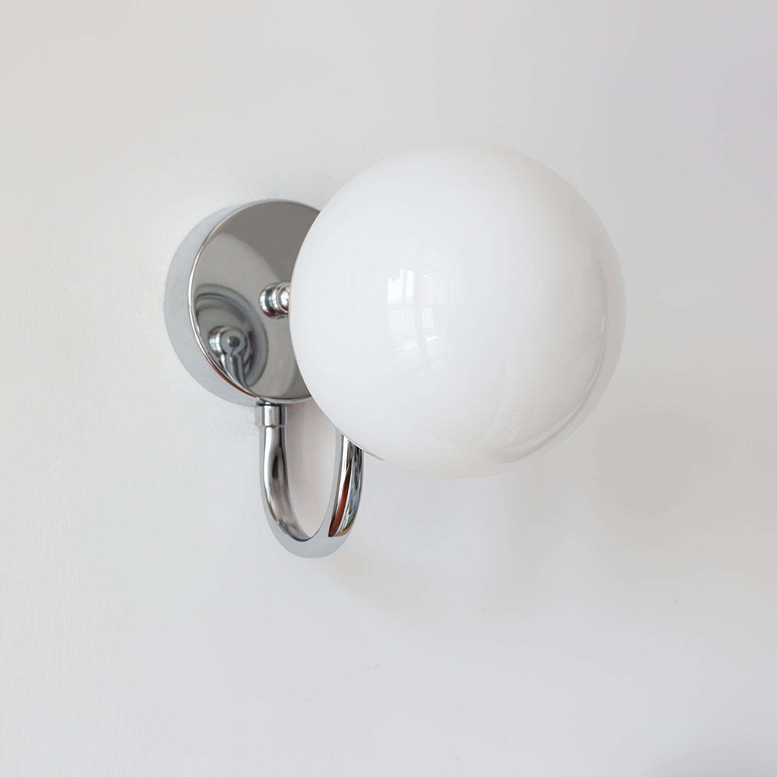 Close angled white glass globe in front of a chrome-coloured round wall plate, with U-shaped arm visible underneath