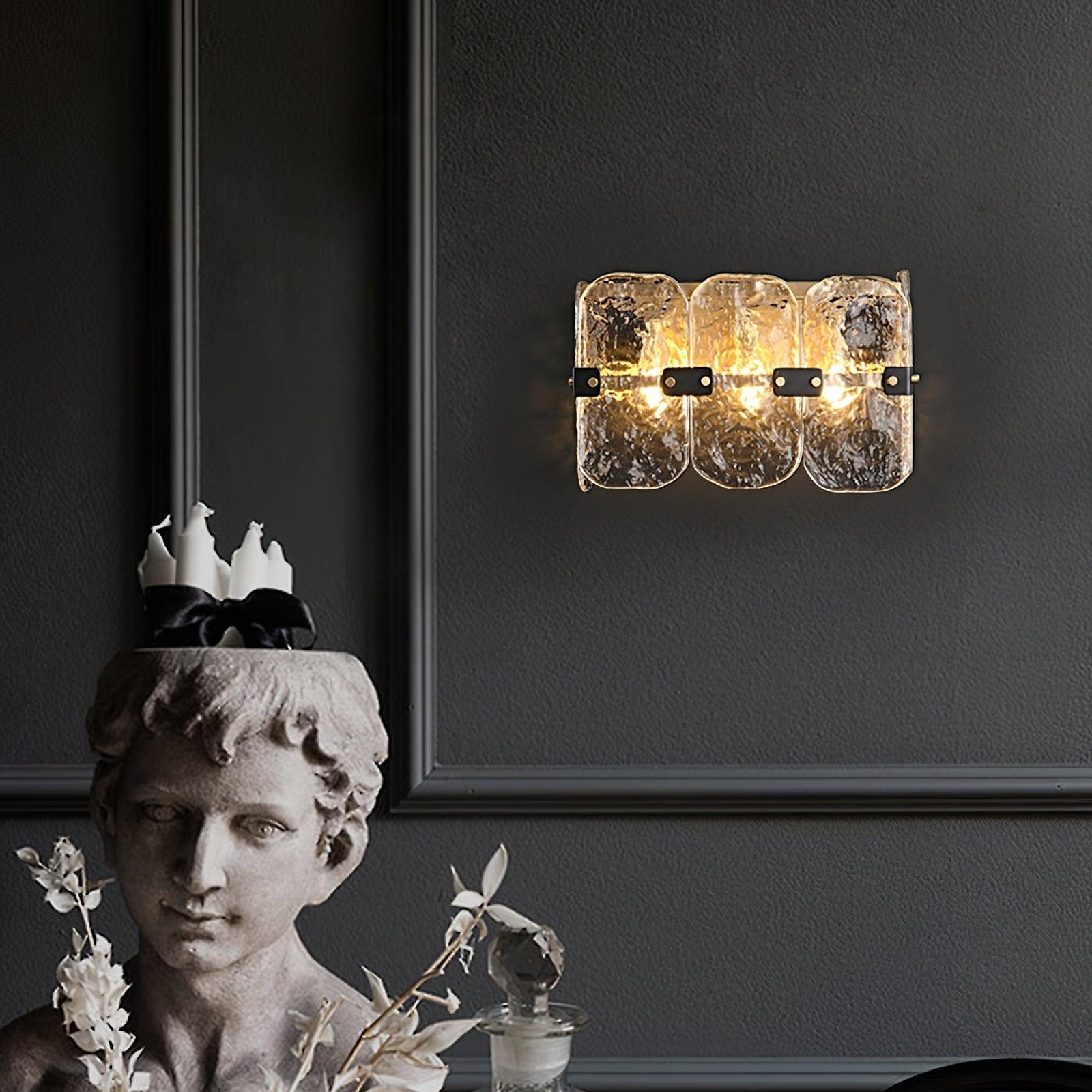 Lit clear-glass sconce above a decorative bust