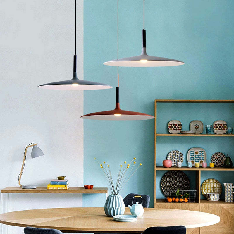 Three shallow dome pendant lights above a dining table beside turquoise walls and a display shelf