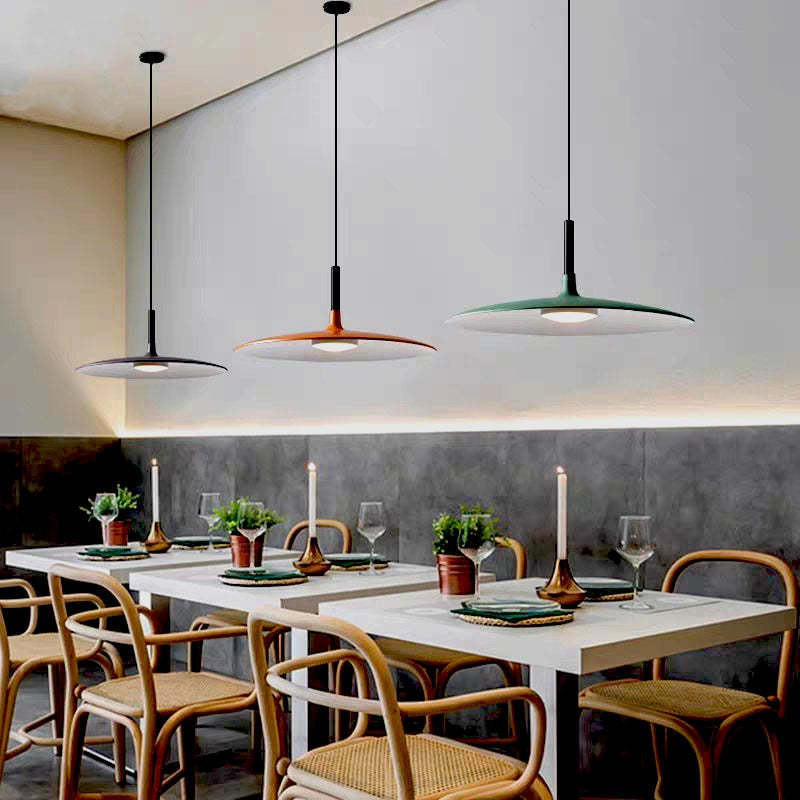 Three colored shallow dome pendants on separate cords and ceiling plates above set dining tables