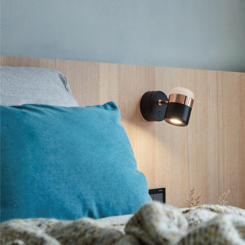 Angled black and copper-coloured wall light beside a bed with a turquoise cushion