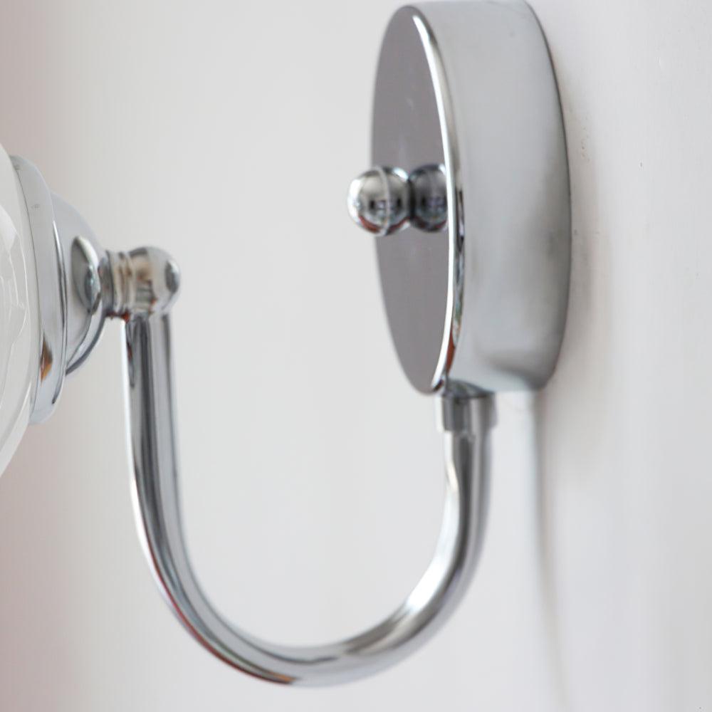 Detail of chrome-coloured U-shaped arm beneath the round plate, with part of the white globe at left